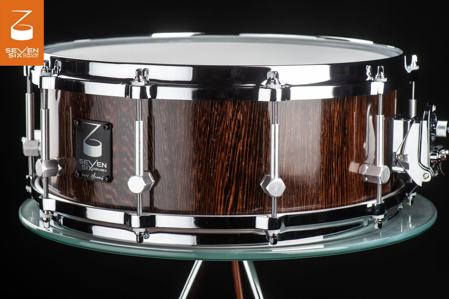 Handmade snare drum featuring a glossy dark wood grain shell, chrome hoops, and brushed hexagonal lugs.