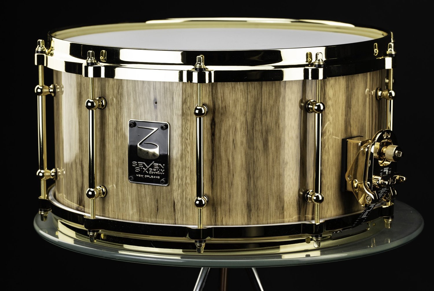 Handmade snare drum featuring a glossy natural wood shell with polished gold hoops, tube lugs, and throw-off.