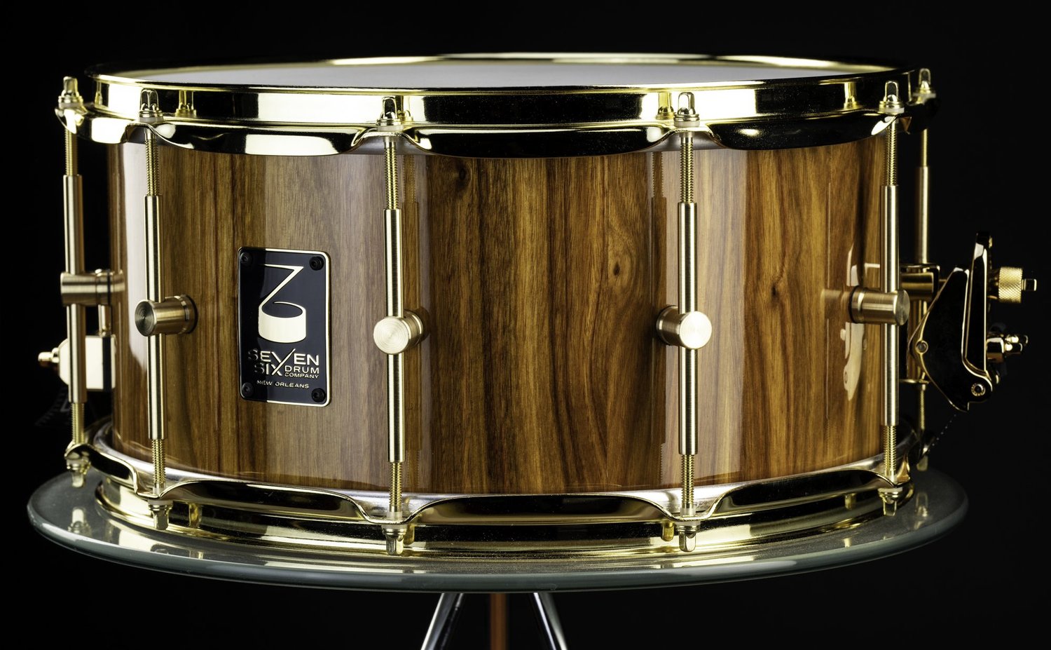 Handmade snare drum featuring a high-gloss natural wood shell, polished brass tube lugs, and gold hoops.