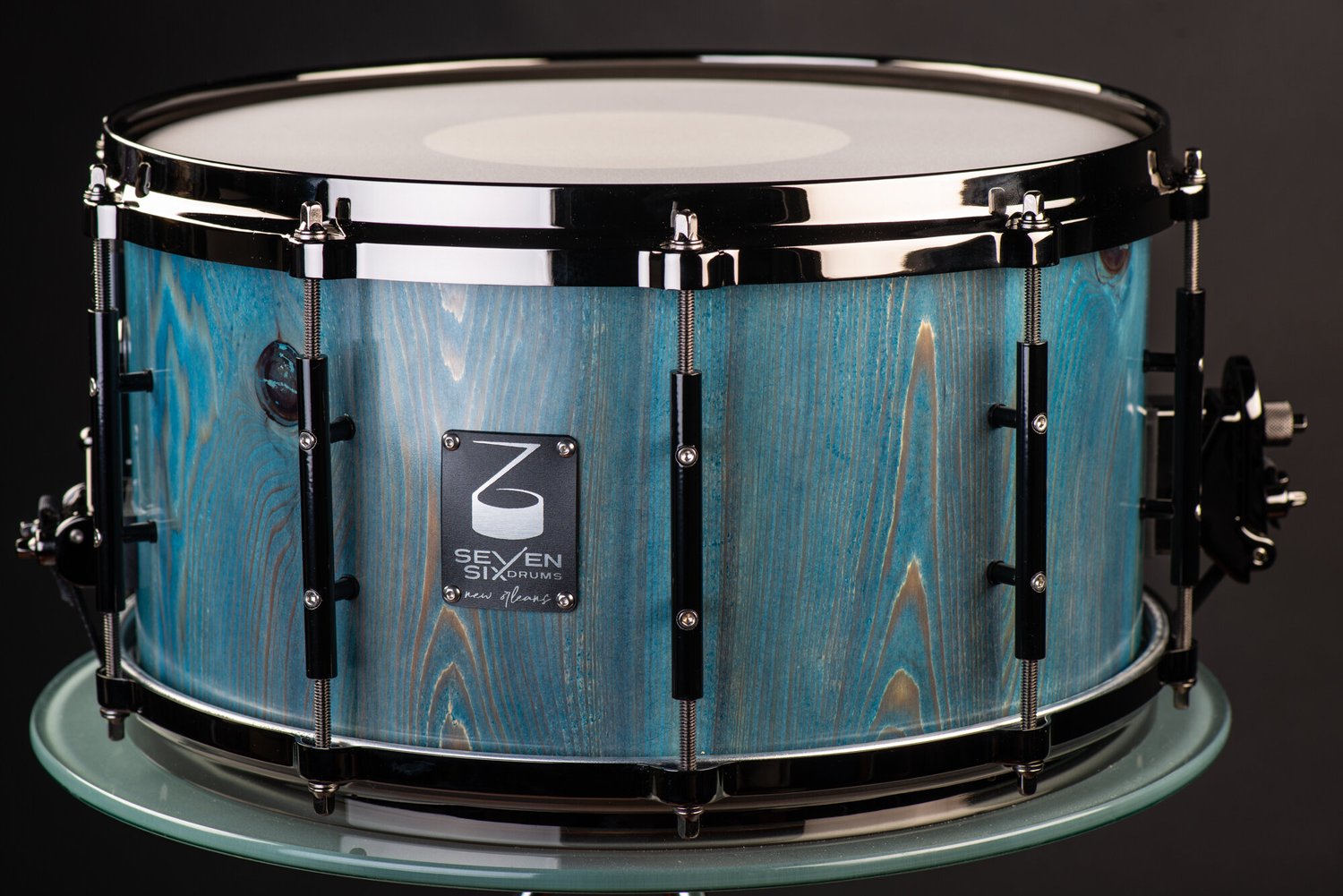 Handmade snare drum with a blue-stained wood grain shell, polished black hoops, and black tube lugs.