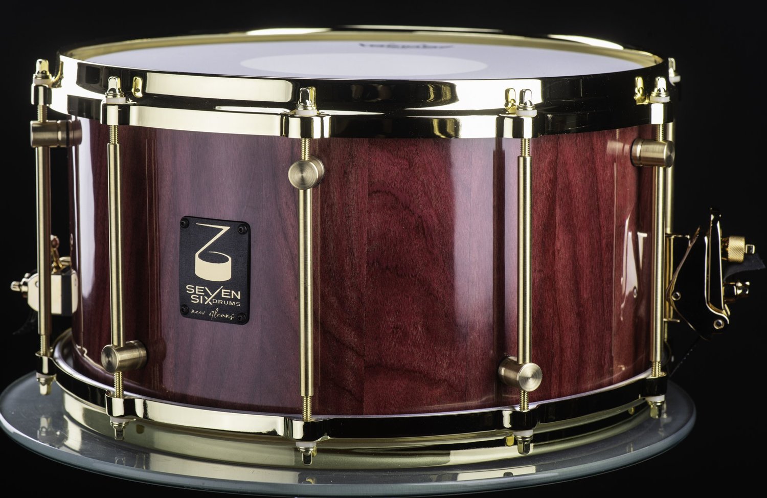 Handmade snare drum with a high-gloss purple wood shell, polished brass hoops, and matching tube lugs.