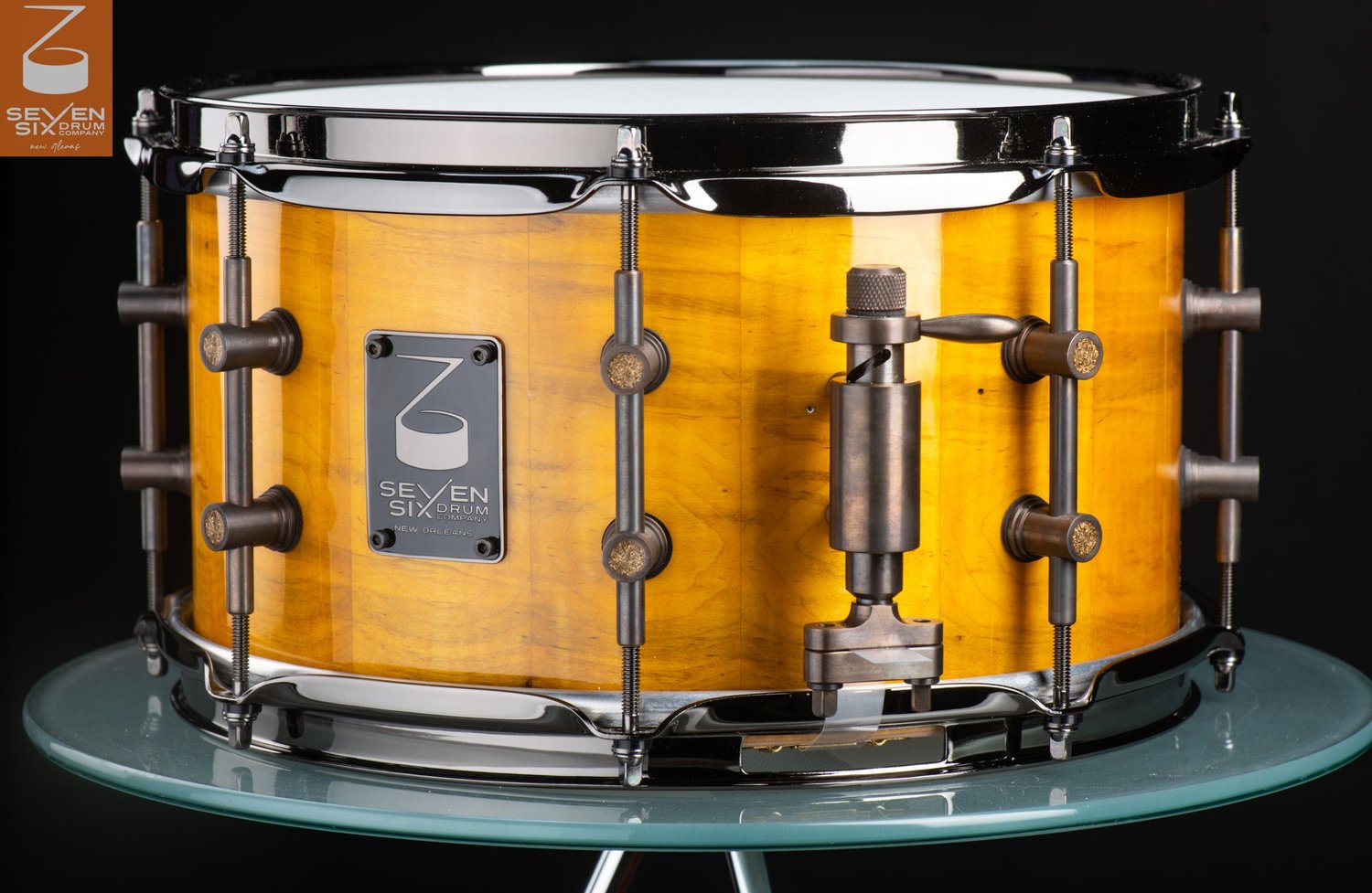 Handmade snare drum featuring a glossy amber wood shell, antique bronze lugs, and matching throw-off.