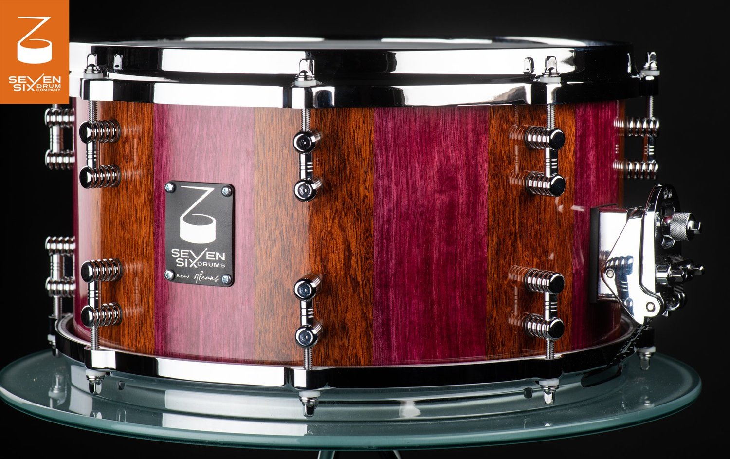 Stave snare drum in glossy alternating purpleheart and brown wood, featuring chrome hoops, lugs, and throw-off.