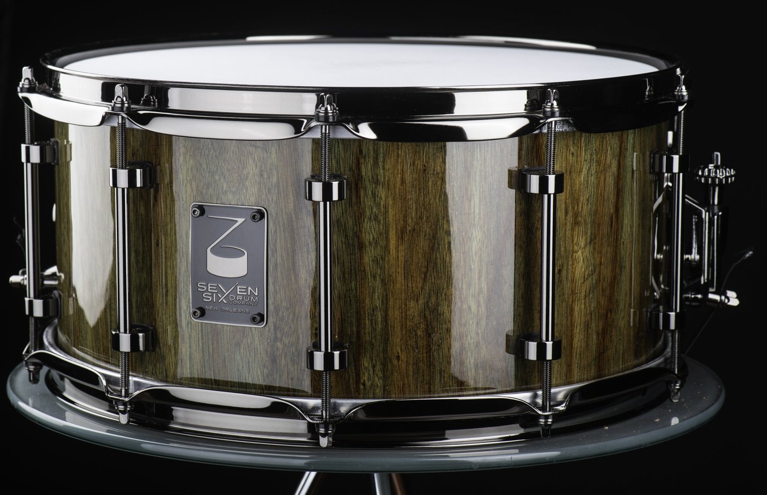 Handmade snare drum featuring a high-gloss natural wood shell with black nickel tube lugs and hoops.