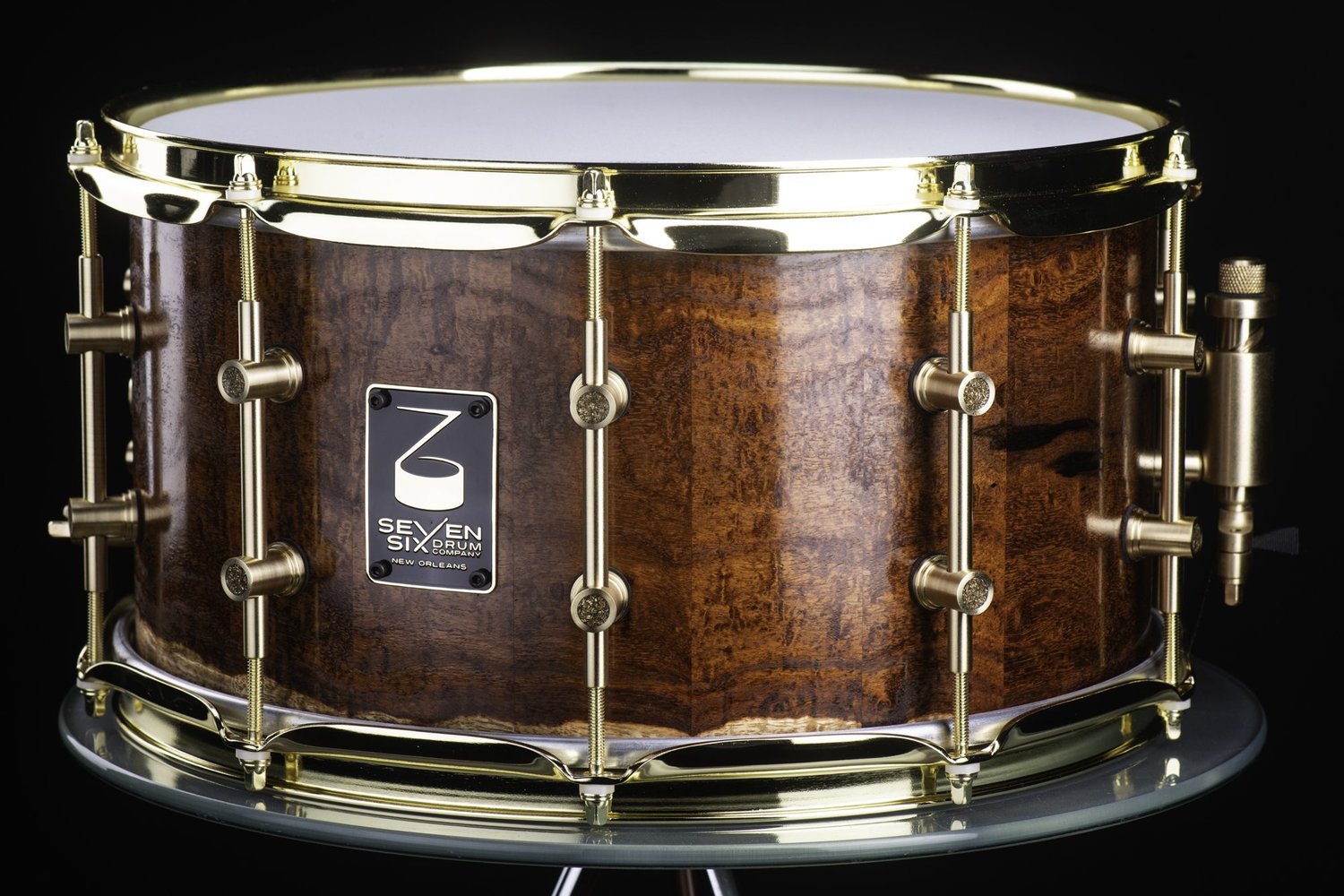Handmade snare drum featuring a glossy figured wood shell, polished brass hoops, and brass tube lugs.