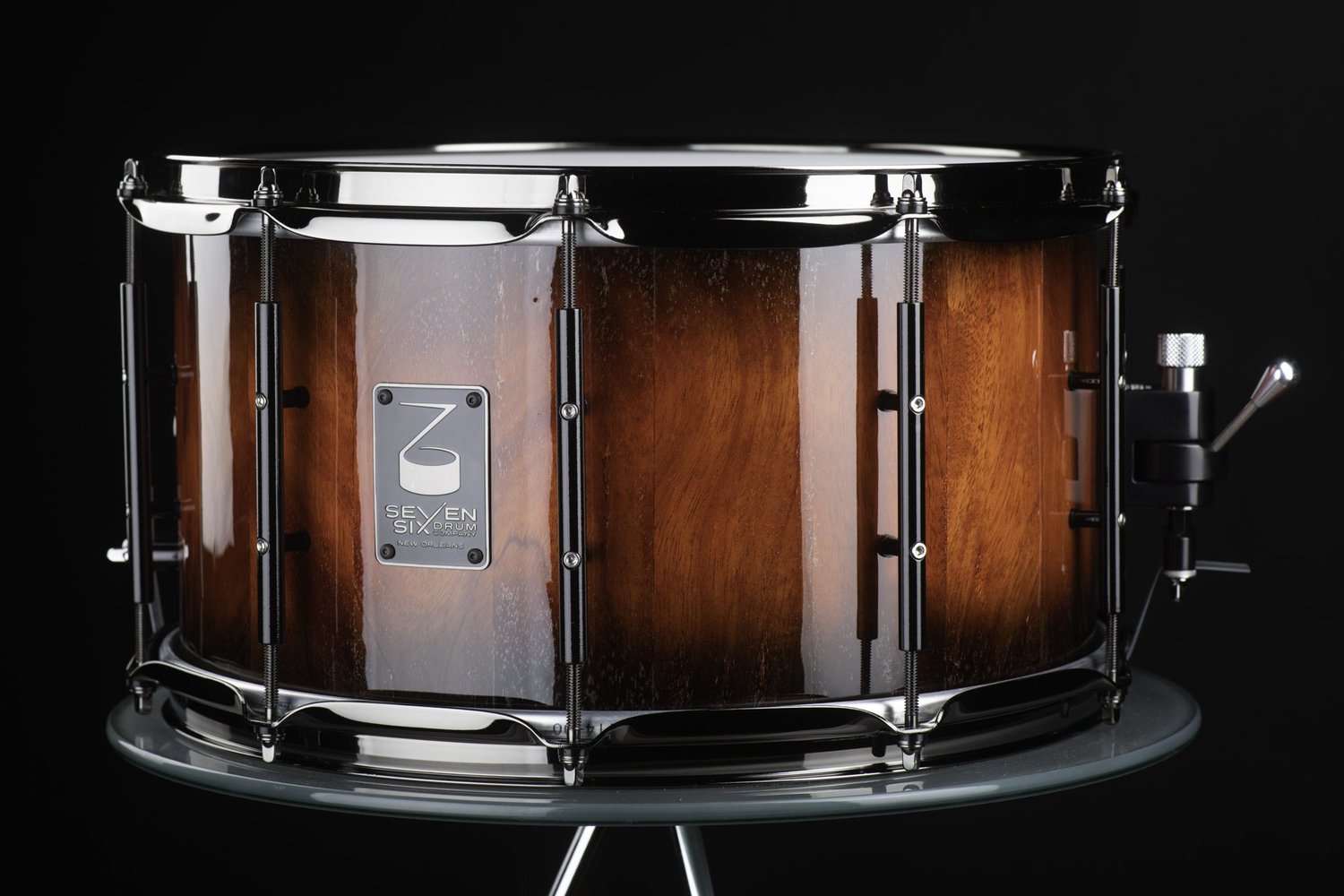 Handmade snare drum with a glossy amber-red wood finish, polished chrome hoops, black tube lugs, and a side throw-off.