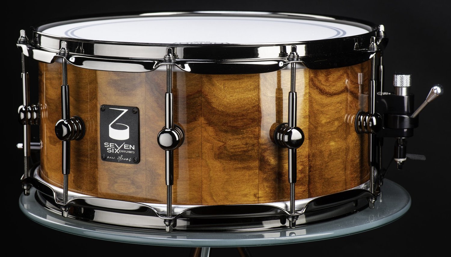 Handcrafted snare drum with a high-gloss wood shell, black nickel hoops, round single-point lugs, and a lever throw-off.