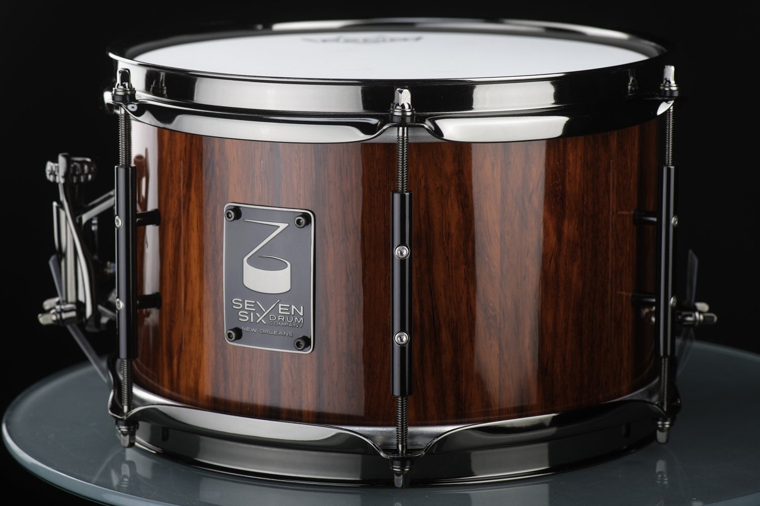 Handmade snare drum with a glossy reddish-brown wood shell, black nickel hoops, and slim black lugs.