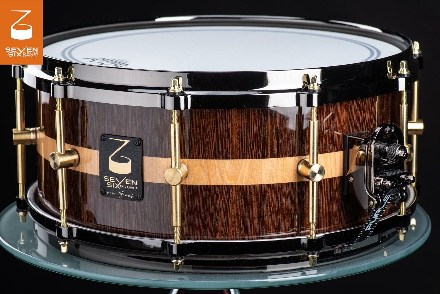 Glossy dark wood snare drum featuring a light center stripe, brass tube lugs, and black nickel hoops.