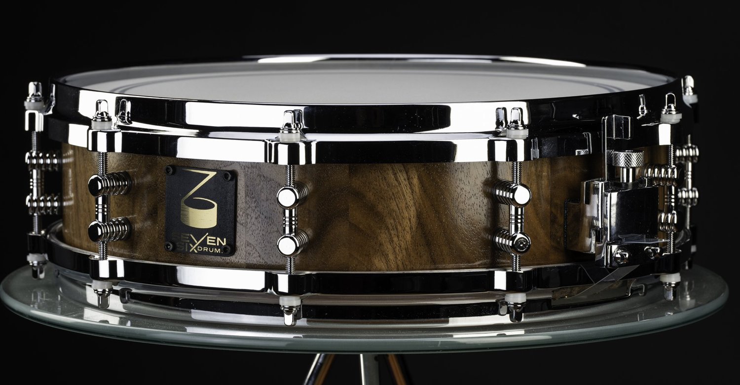 Handmade snare drum featuring a natural walnut shell with polished chrome hoops, tube lugs, and a throw-off.