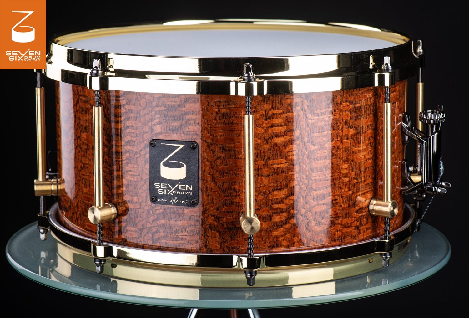 Handmade snare drum with a high-gloss figured wood shell, polished brass hoops, and brass tube lugs.