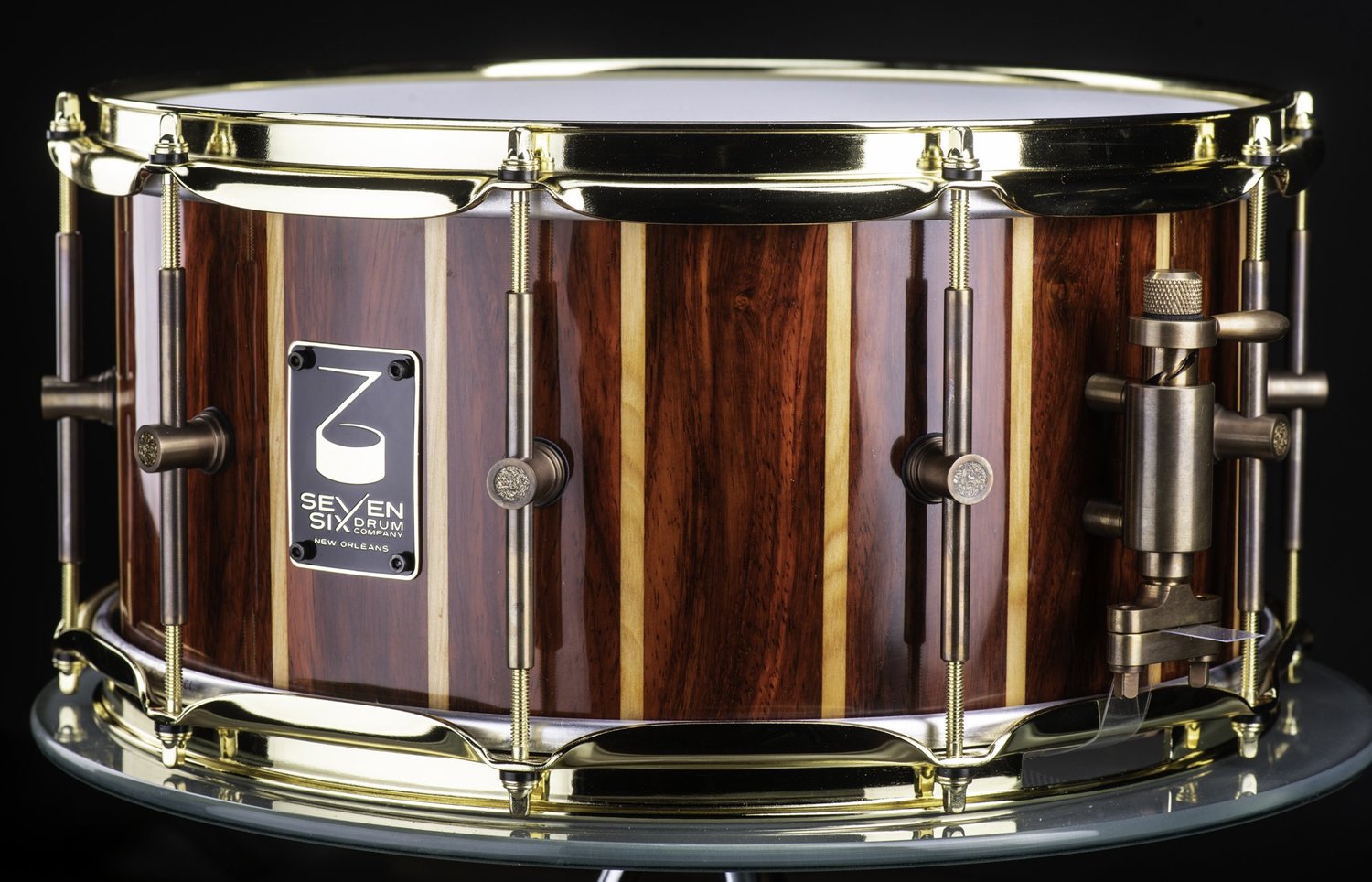 Gloss-finish striped wood snare drum featuring red and blonde vertical staves, polished brass hoops, and bronze lugs.