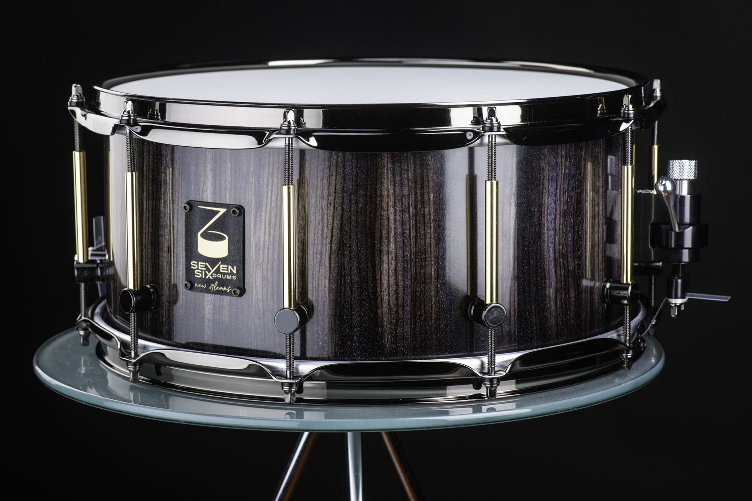 Handmade snare drum featuring a glossy dark wood grain shell, black nickel hoops, and brass tube lugs.