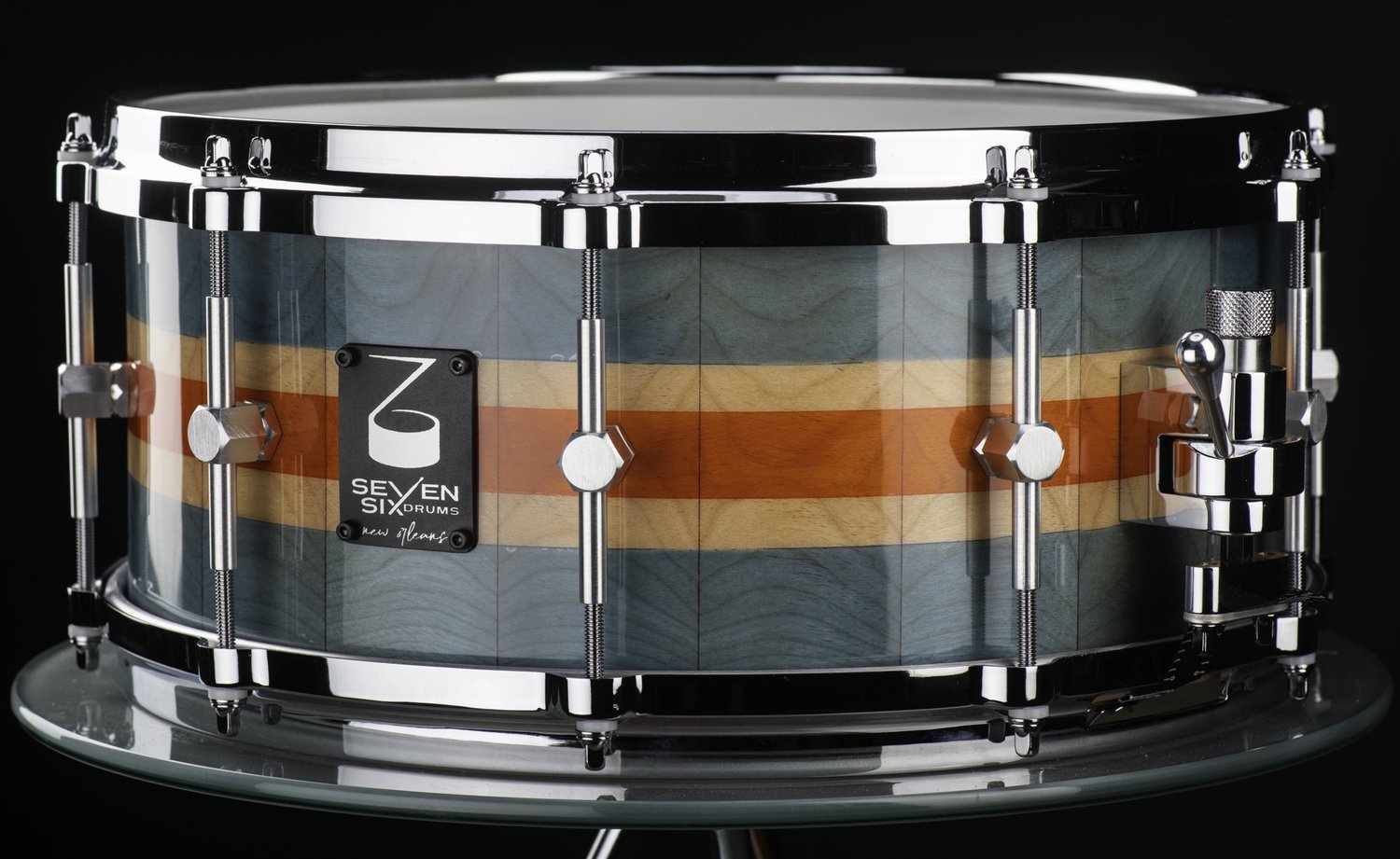 Handmade snare drum with a glossy teal, maple, and orange striped wood shell, chrome hoops, and hex-style lugs.