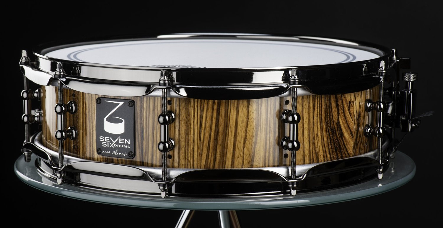 Snare drum featuring a high-gloss zebrawood shell with black nickel hoops and lugs.
