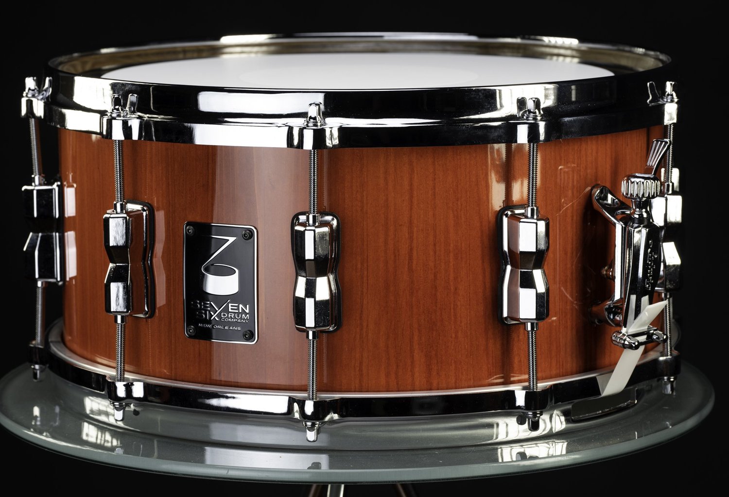 Handmade snare drum with a glossy reddish wood shell, chrome hoops, and polished lugs.