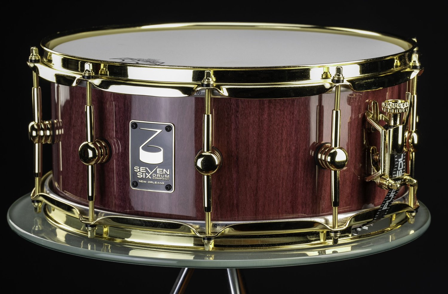 Handmade snare drum with a glossy purple wood shell and polished gold hoops, lugs, and strainer.