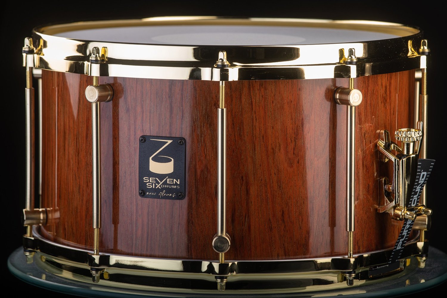 Handmade snare drum with a glossy natural wood shell, polished brass hoops, and brass tube lugs.