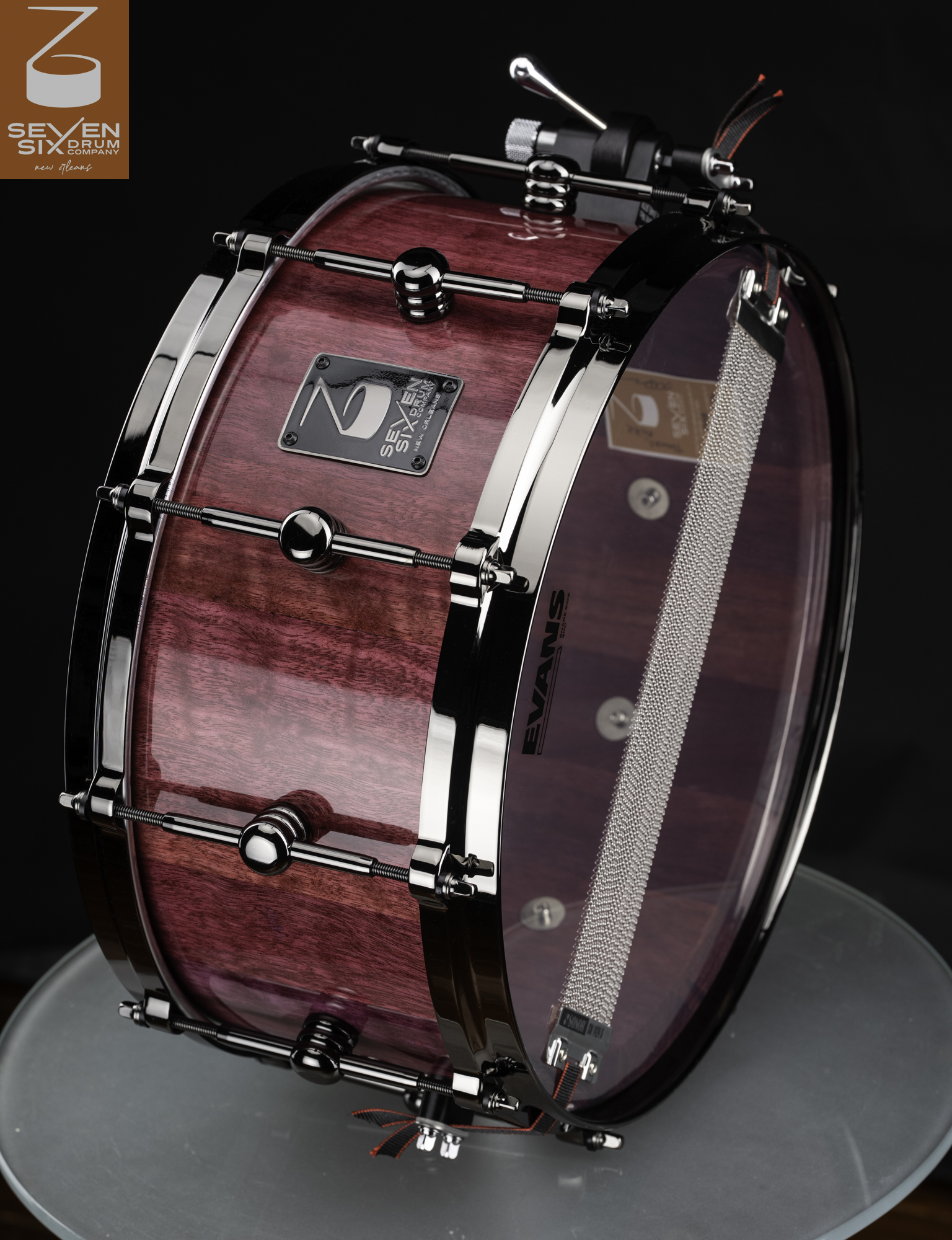 Gloss-finished purple wood snare drum with black nickel hardware, round lugs, and visible snare wires.