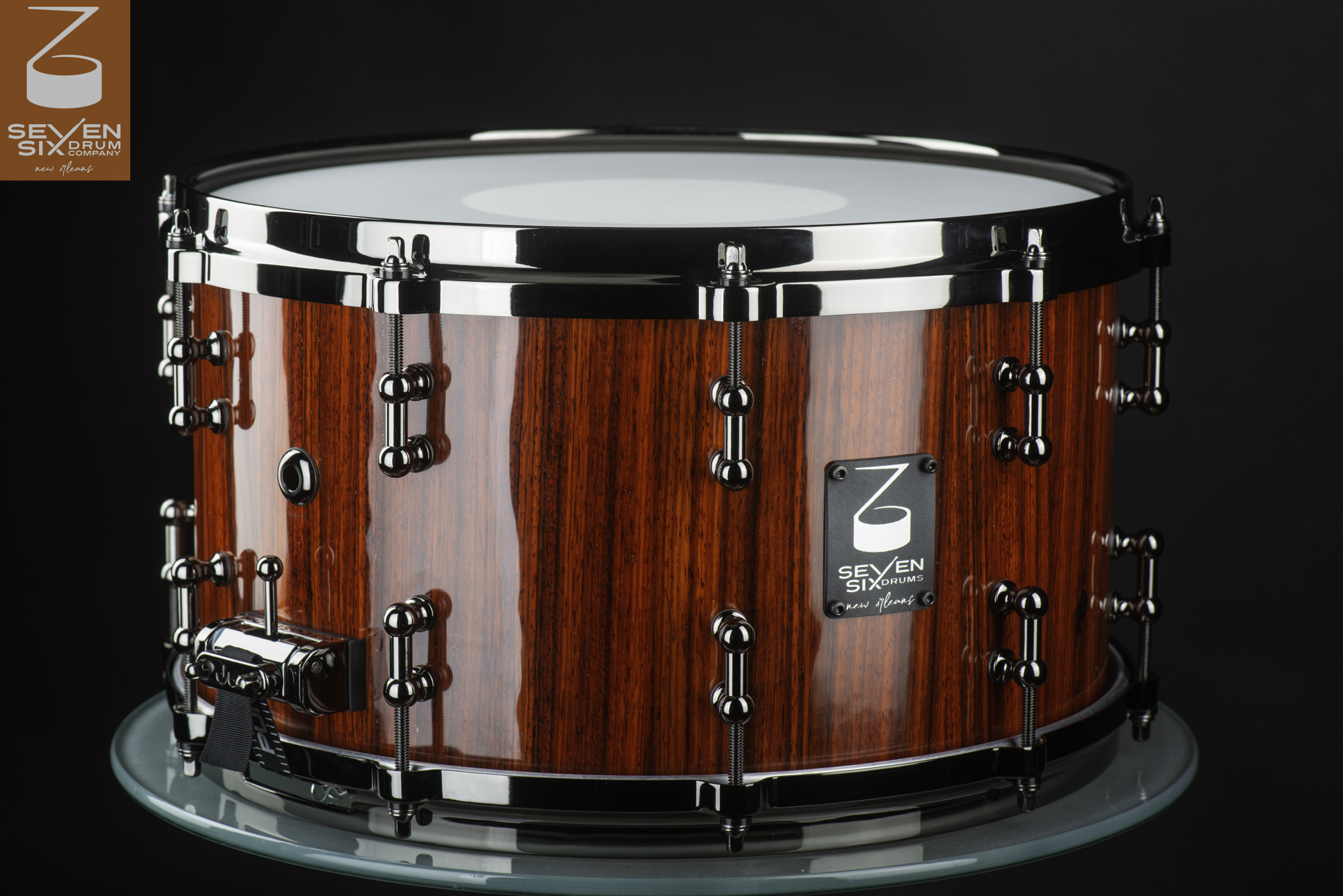 Handmade snare drum with a glossy red vertical-grain wood shell, black nickel tube lugs, and dark chrome hoops.