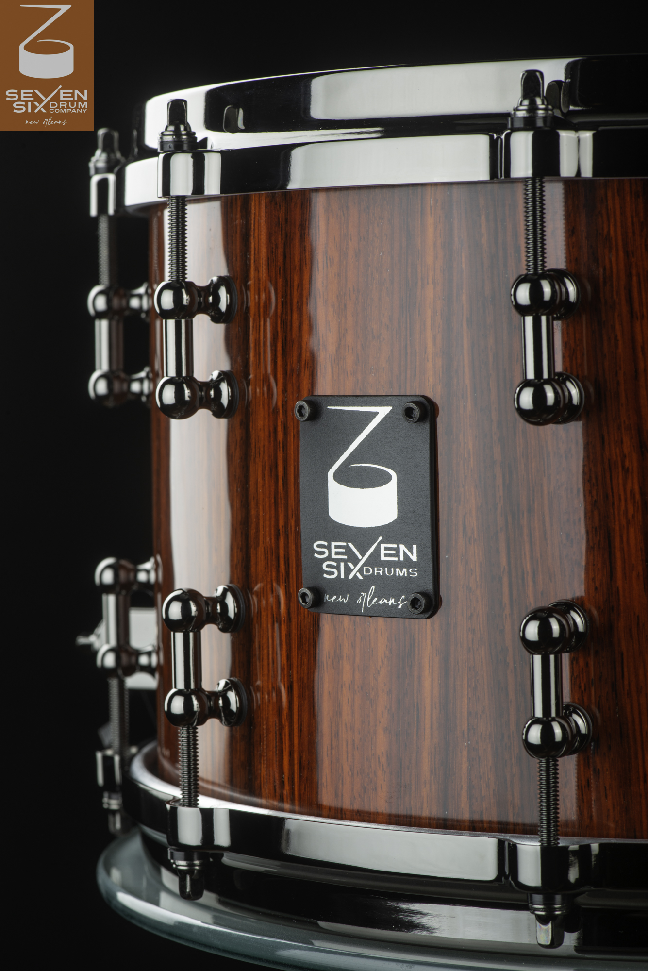 Handmade snare drum featuring a glossy reddish-brown wood shell with black nickel tube lugs and hoops.