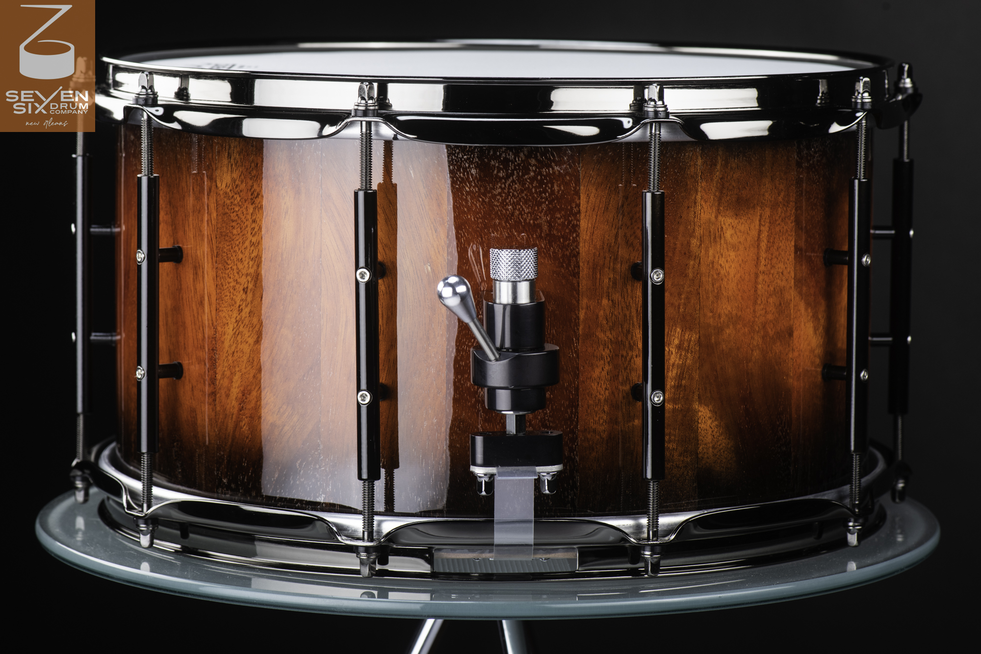 Glossy reddish-brown wood snare drum featuring chrome hoops, black tube lugs, and a metal throw-off strainer.