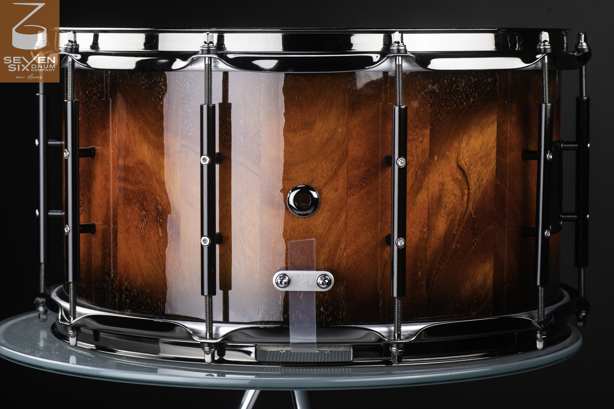 Handmade wooden snare drum in a glossy reddish-brown burst finish with black tube lugs and chrome hoops.