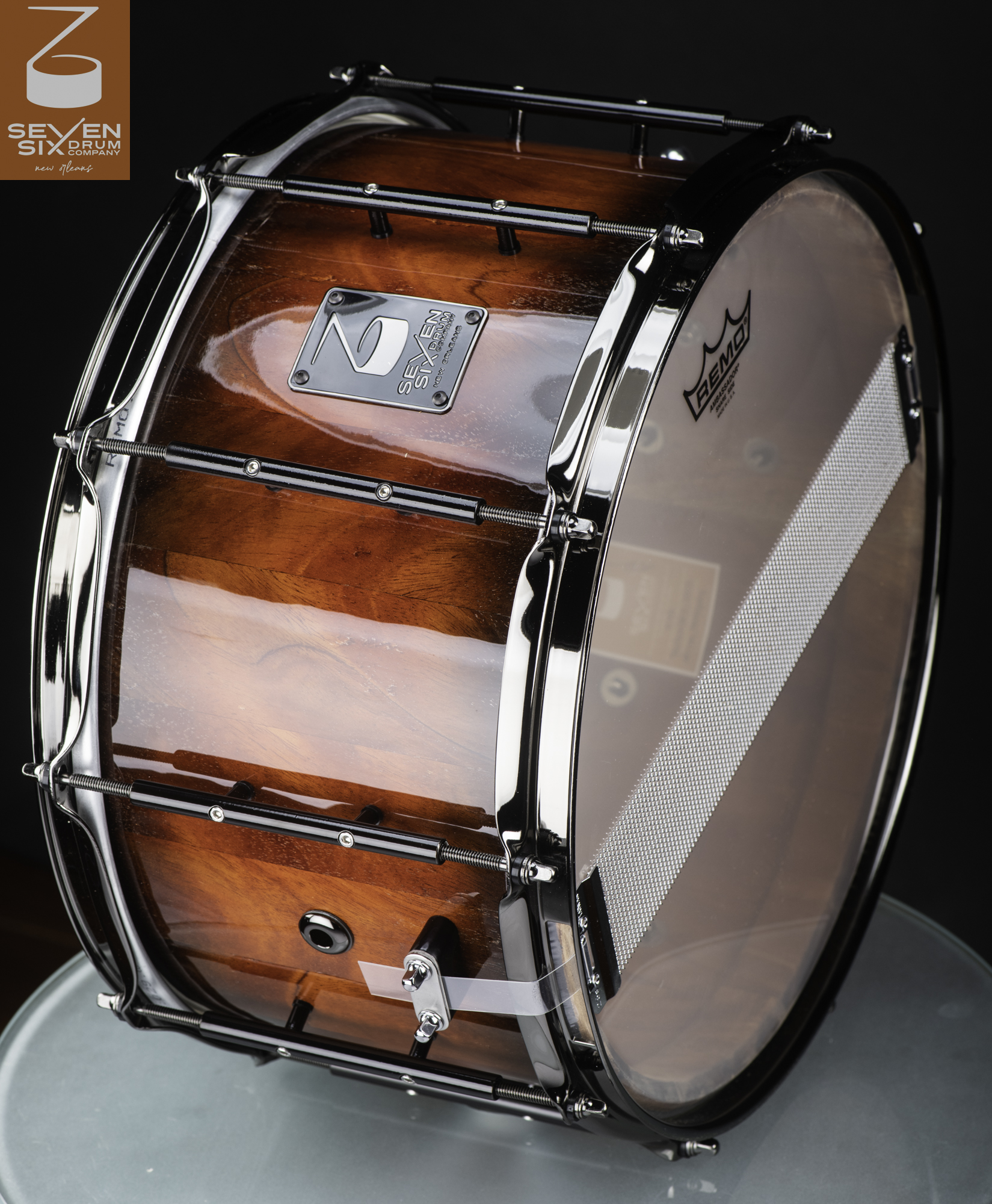 Deep wooden snare drum in a high-gloss amber finish, fitted with black tube lugs, chrome hoops, and snare wires.