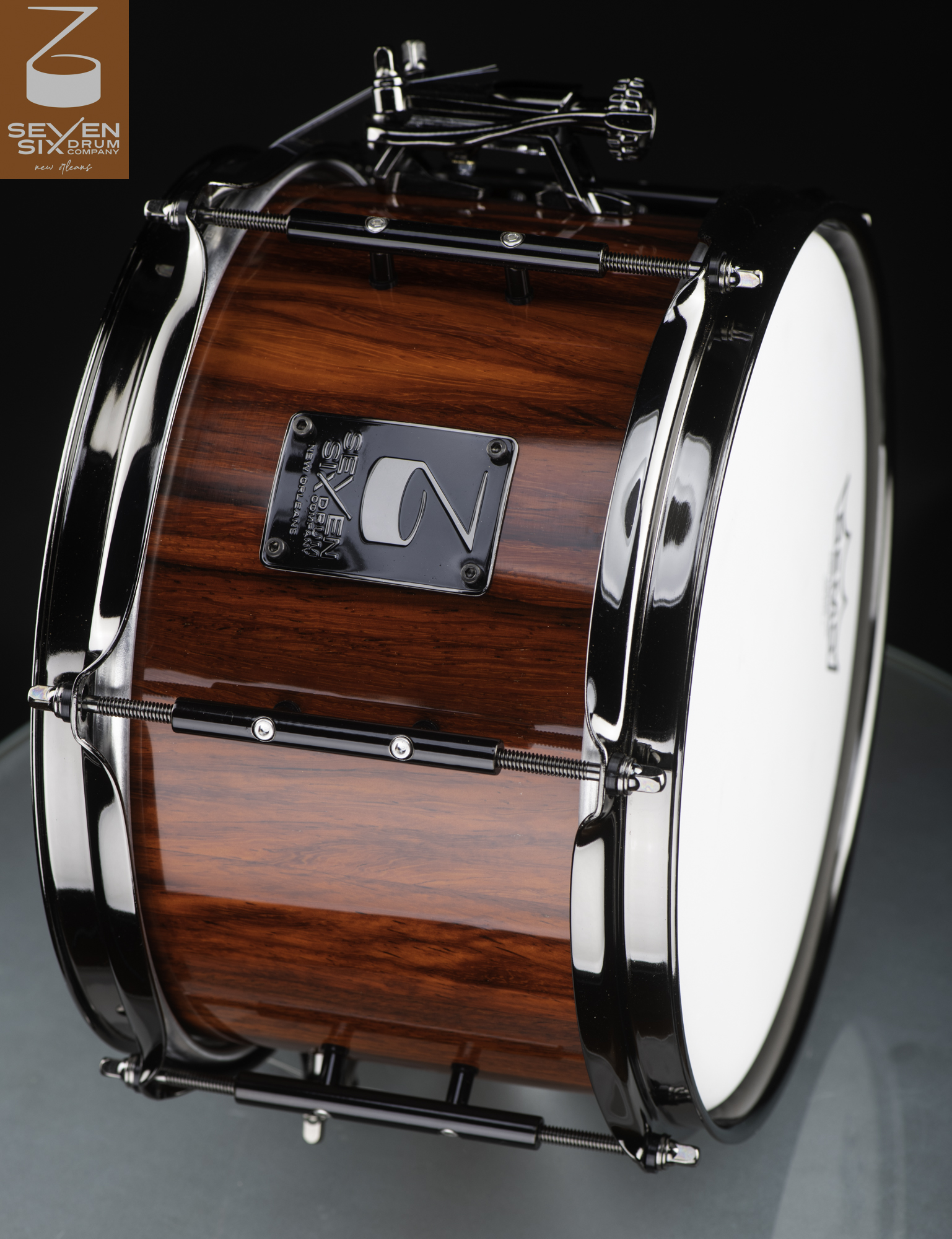 Handmade wooden snare drum featuring a glossy red-brown grain finish, black nickel hoops, and black tube lugs.