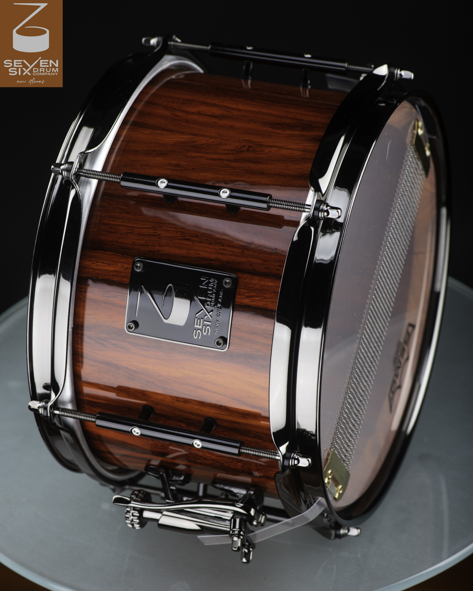 Handmade snare drum featuring a glossy reddish-brown wood shell, black nickel hoops, and tube lugs.