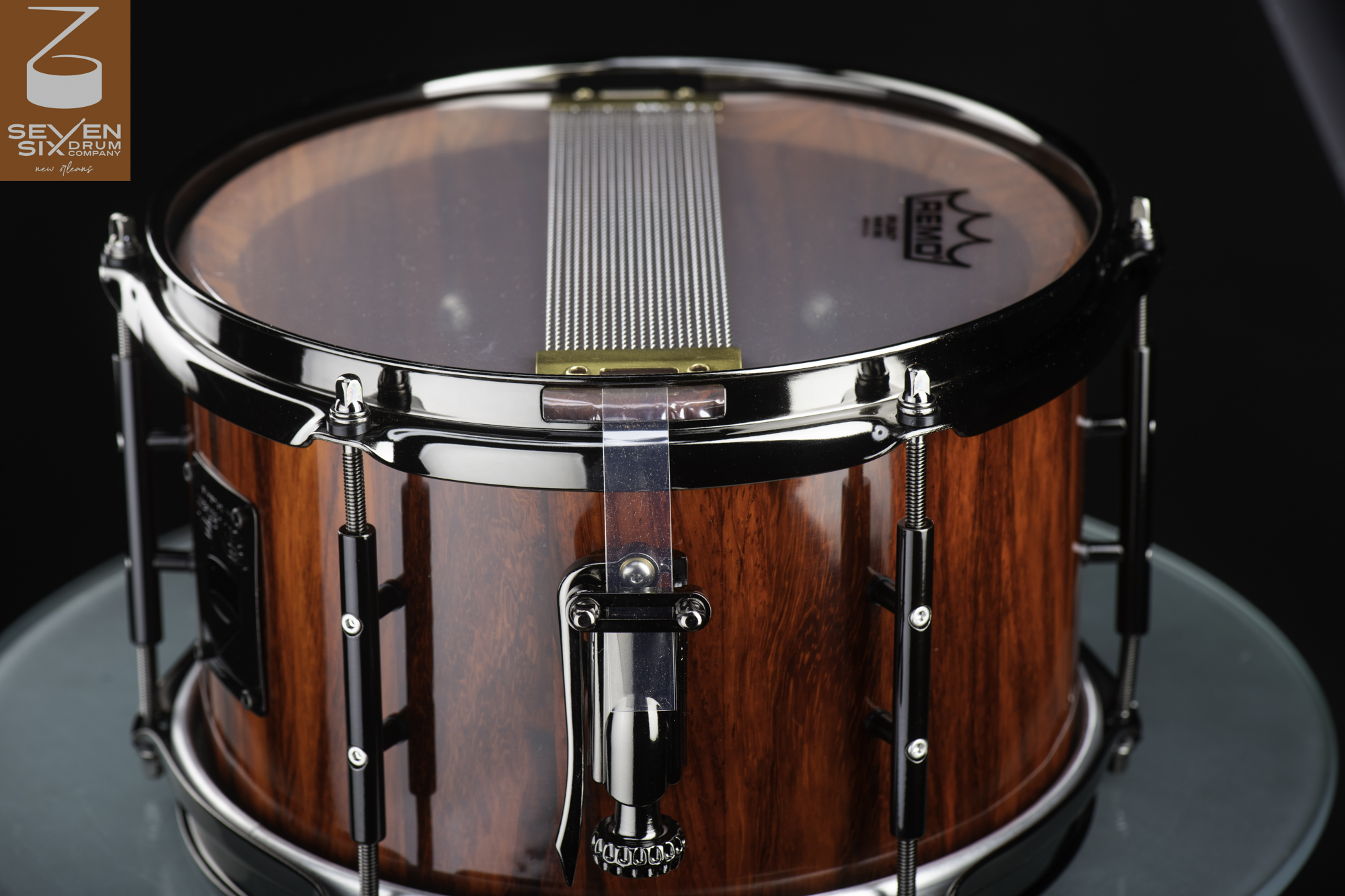 Handmade snare drum featuring a glossy red wood grain shell, black nickel hoops and lugs, and bottom snare wires.