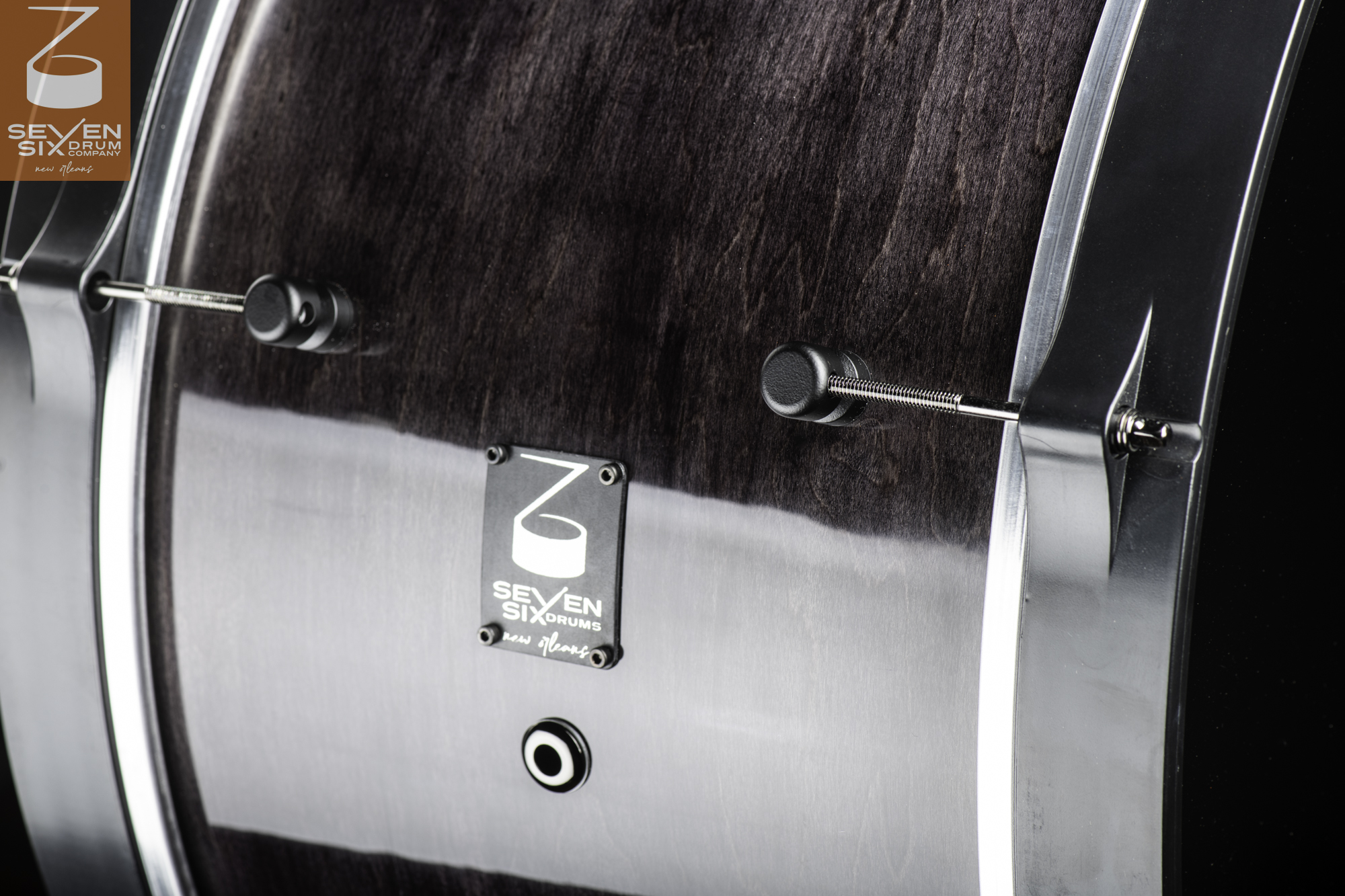 Glossy dark wood snare drum shell featuring black hoop claws, threaded tension rods, round lugs, and a logo badge.
