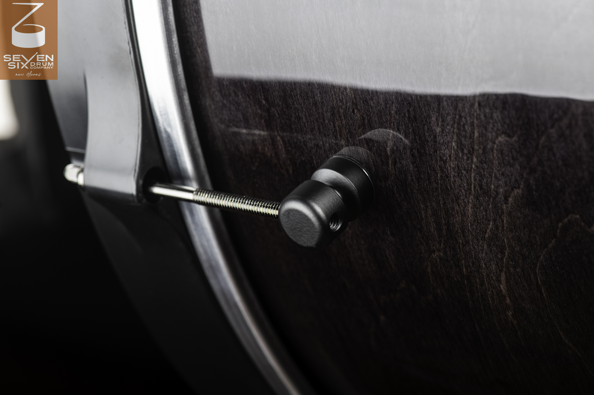 A gloss-finished dark wood snare drum shell features a matte black lug, metal tension rod, and black hoop.