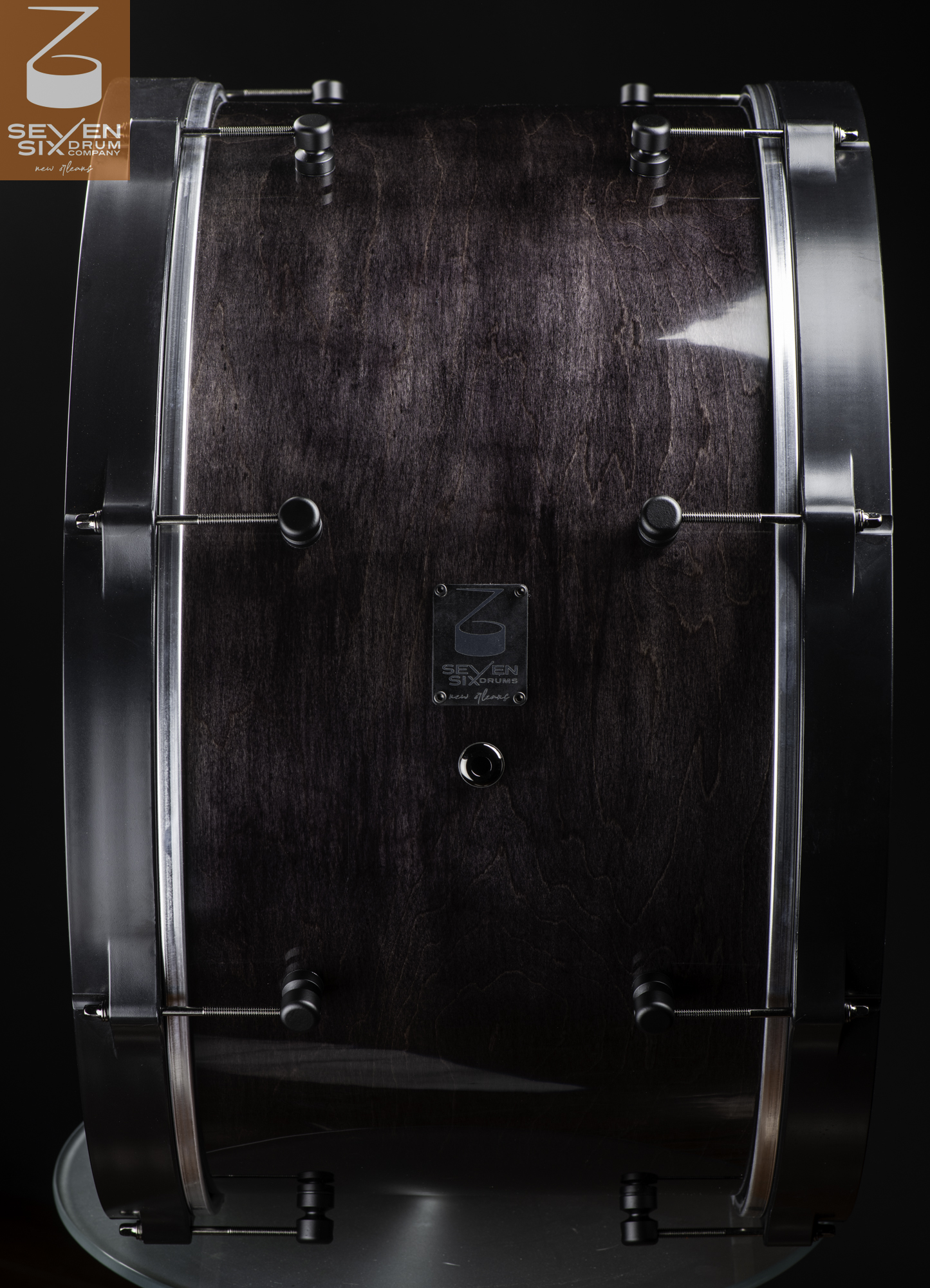 Handmade bass drum with a glossy dark-stained wood shell, round black lugs, and matching black hoops.