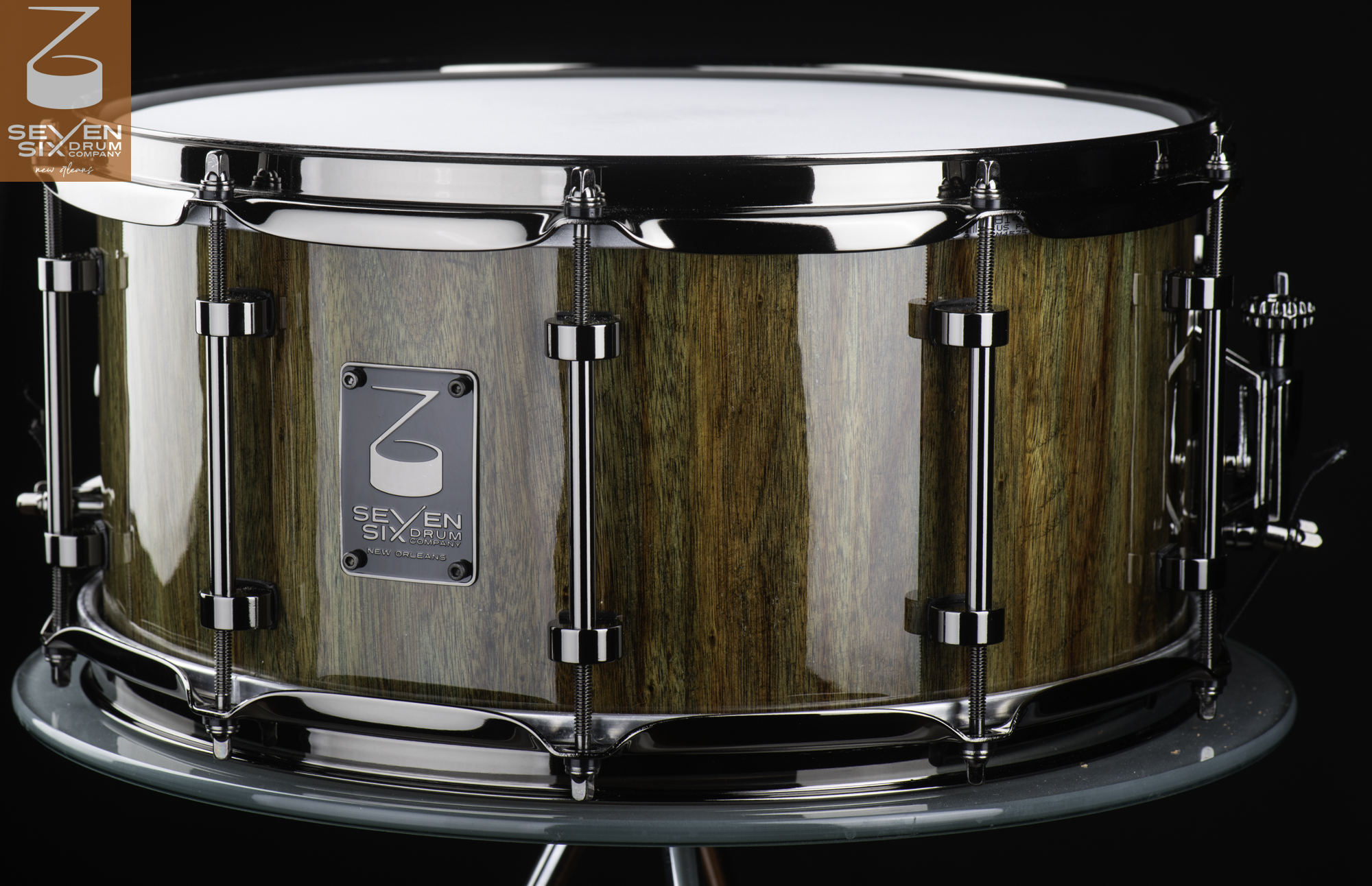 Handmade snare drum featuring a glossy striped wood shell, polished chrome tube lugs, and triple-flanged hoops.