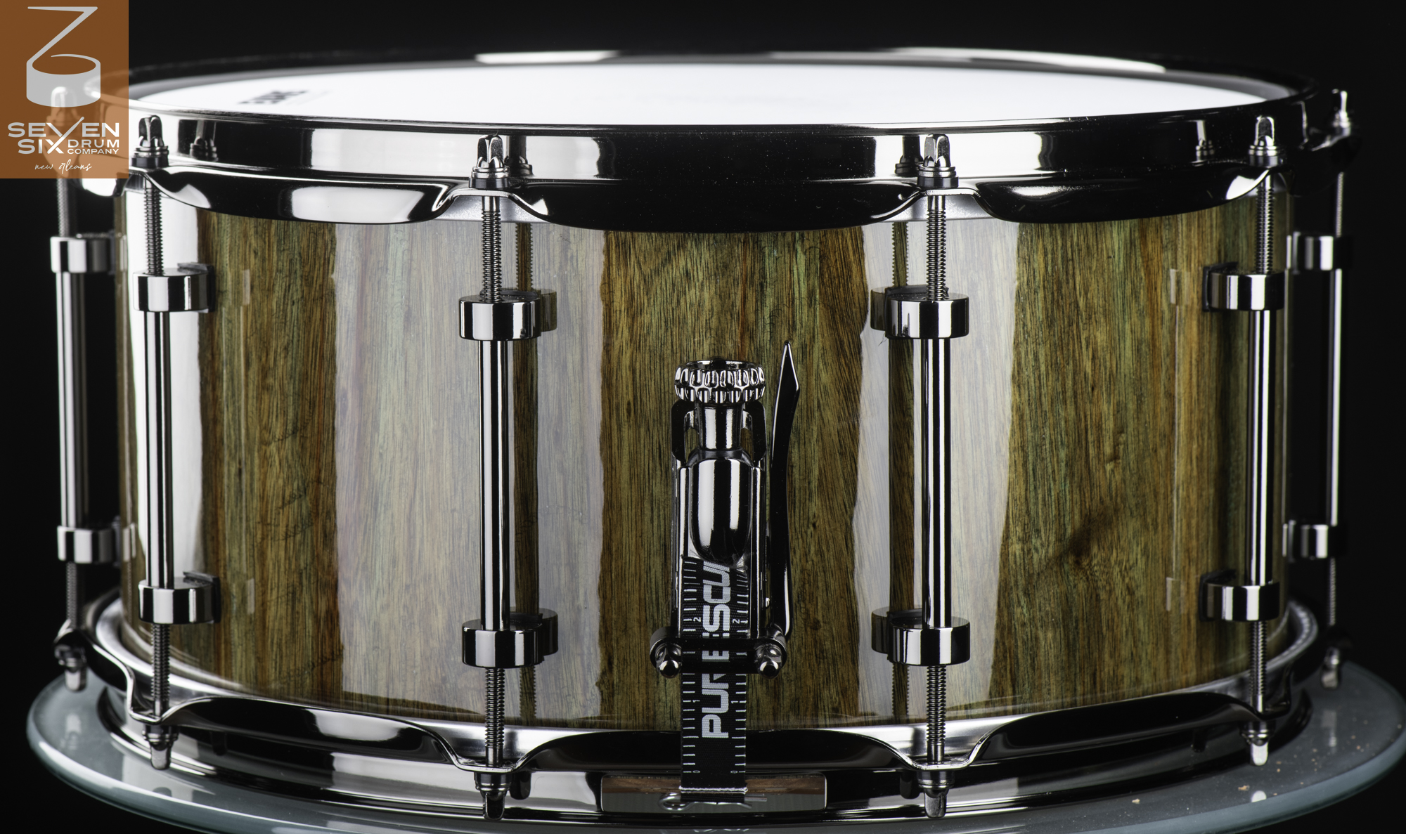 Handmade snare drum featuring a glossy vertical-grain wood shell, polished chrome tube lugs, and a snare throw-off.