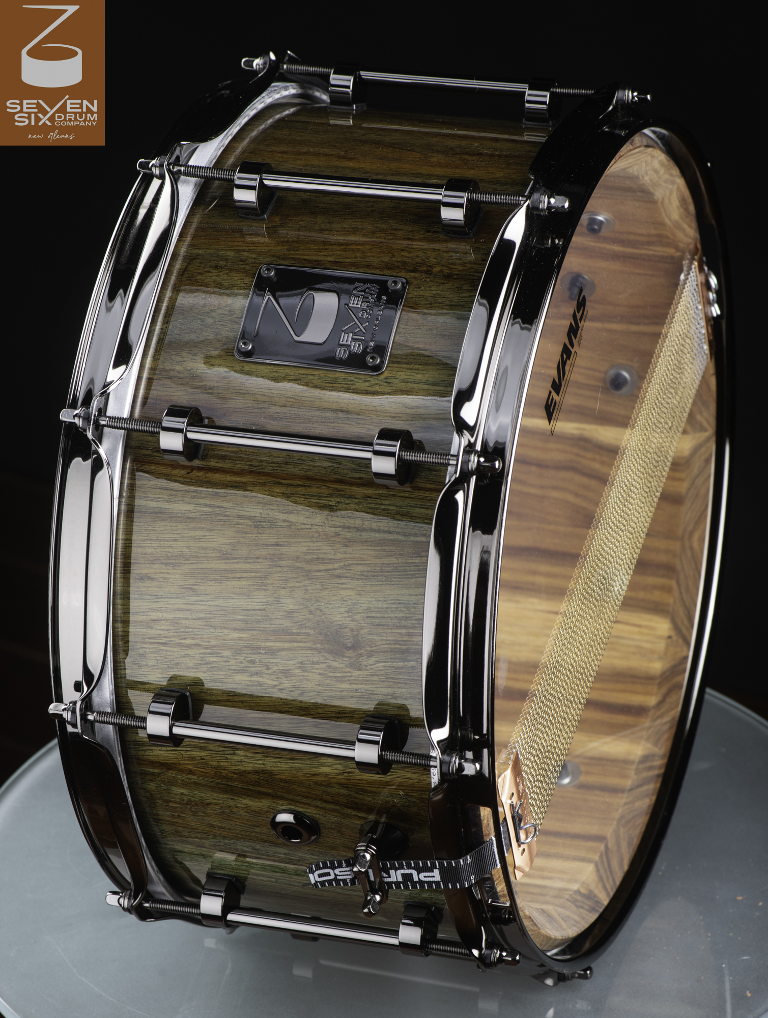 Handmade wood snare drum with a high-gloss natural finish, black chrome tube lugs, and brass snare wires.