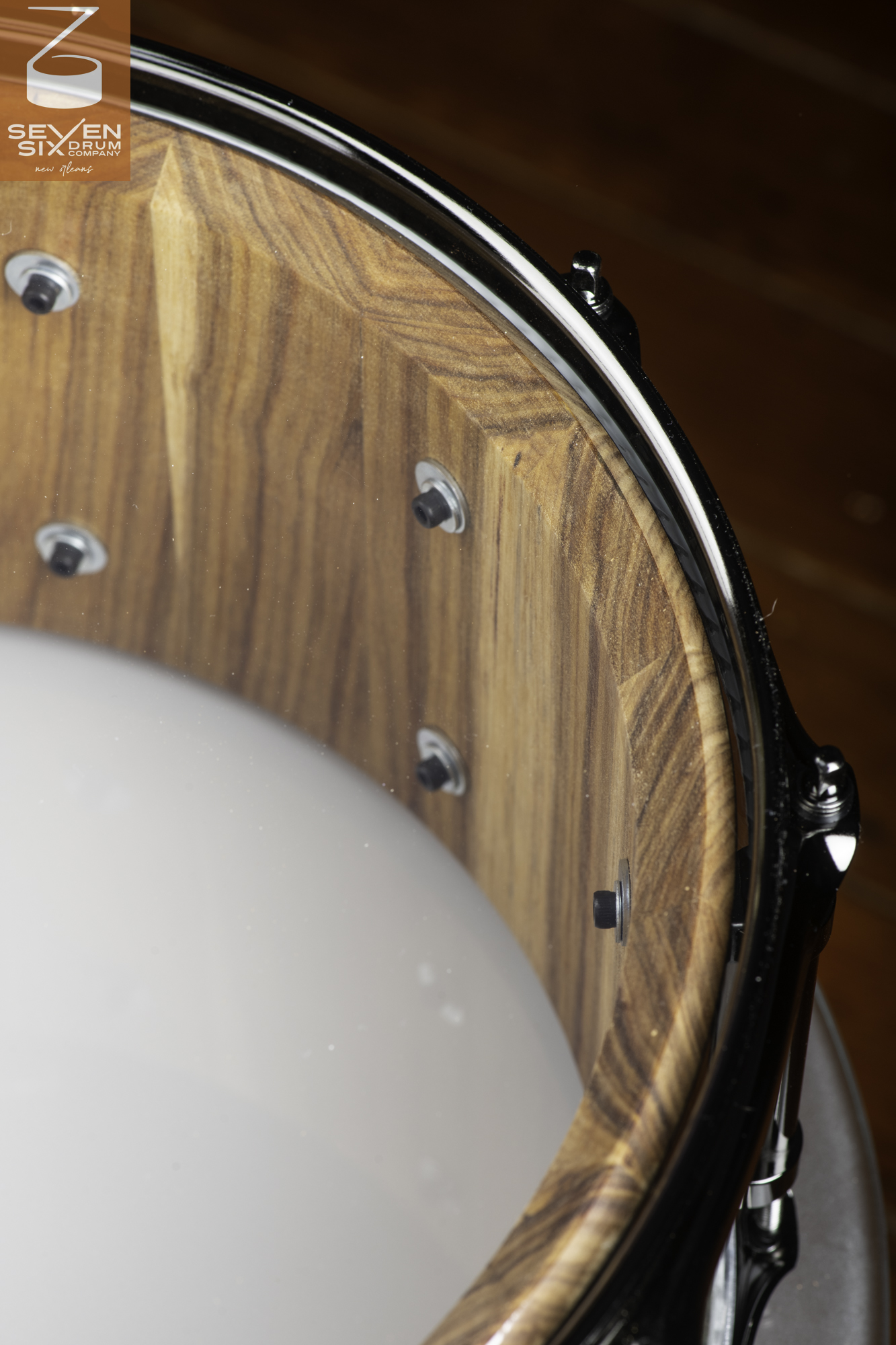Interior of a natural-finish stave wood snare drum shell with prominent grain, internal mounting screws, and a black metal hoop.