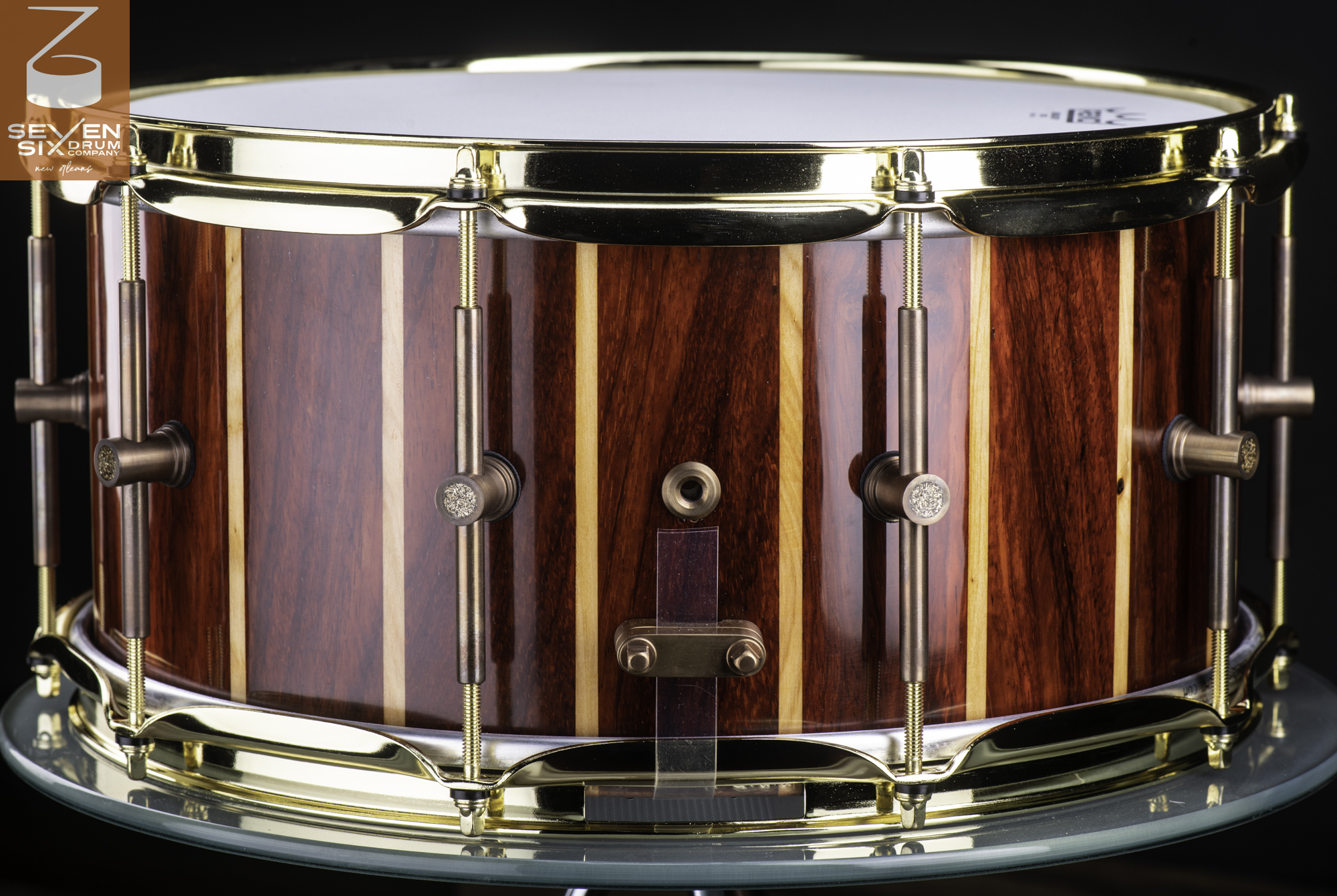 Glossy red and blonde striped wood snare drum with polished brass hoops and bronze tube lugs.