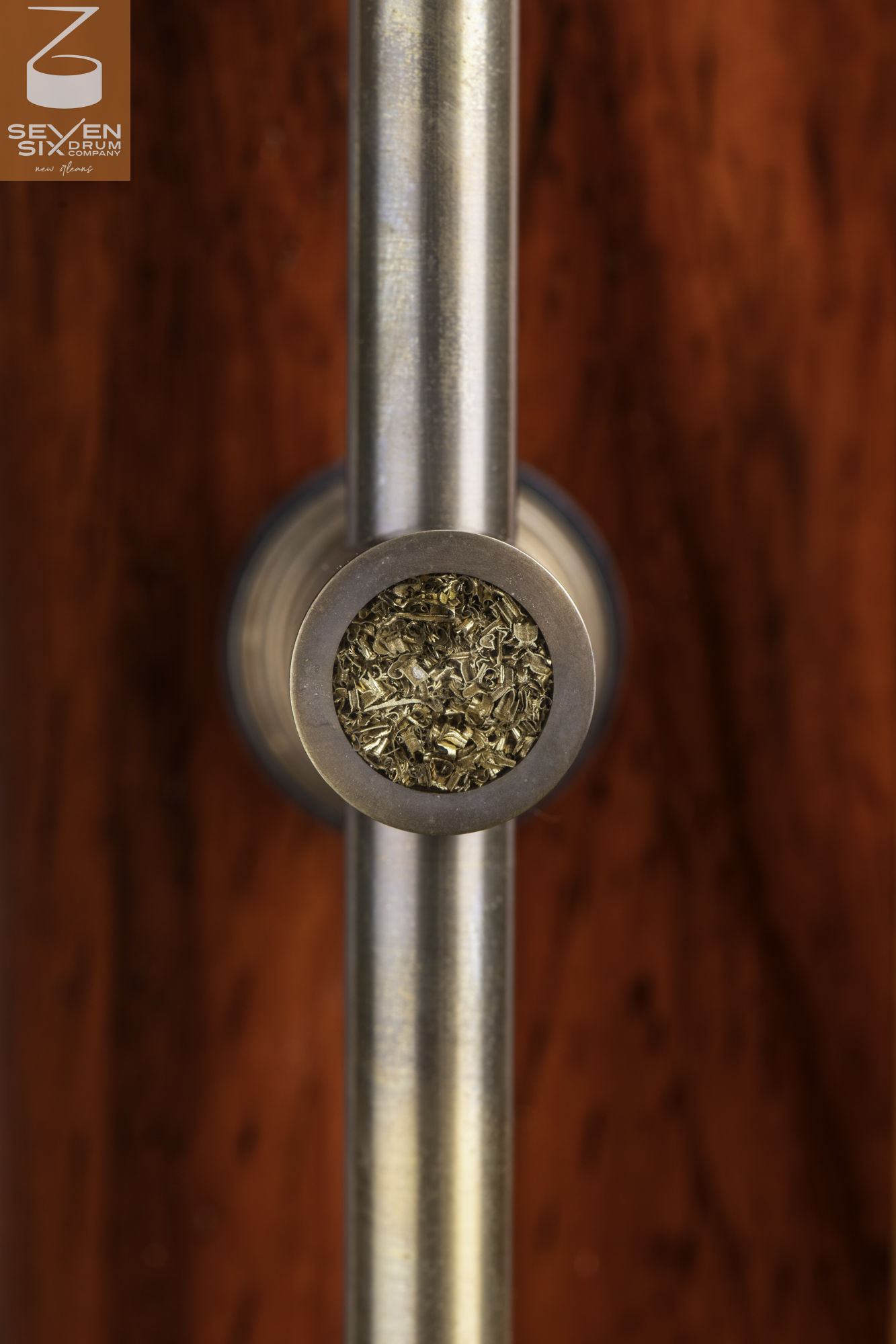 Brushed metal tube lug with a brass shavings inlay mounted on a vibrant red wood drum shell.