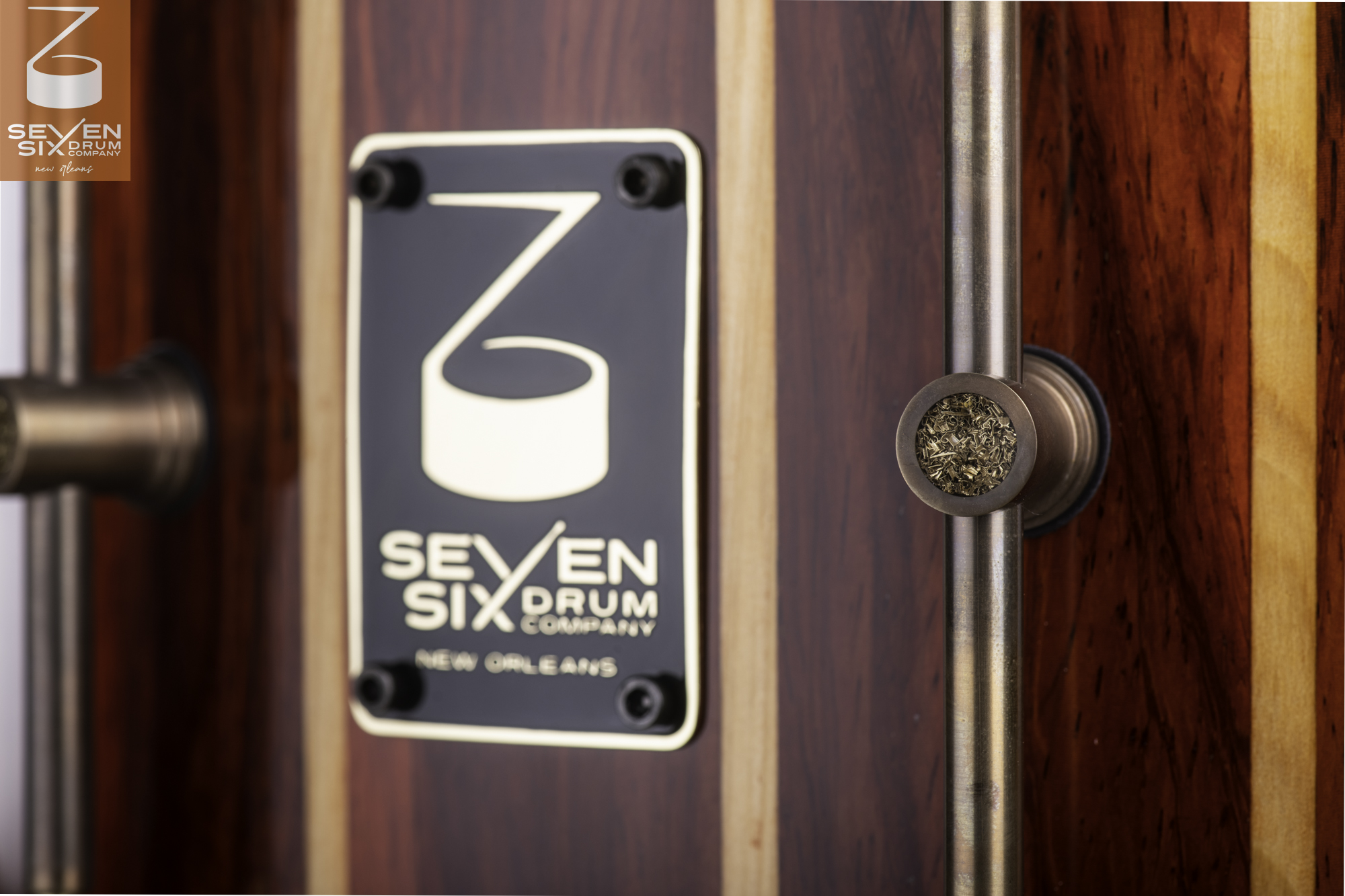 High-gloss striped wood snare drum shell featuring an antique brass tube lug and black Seven Six Drum Company badge.