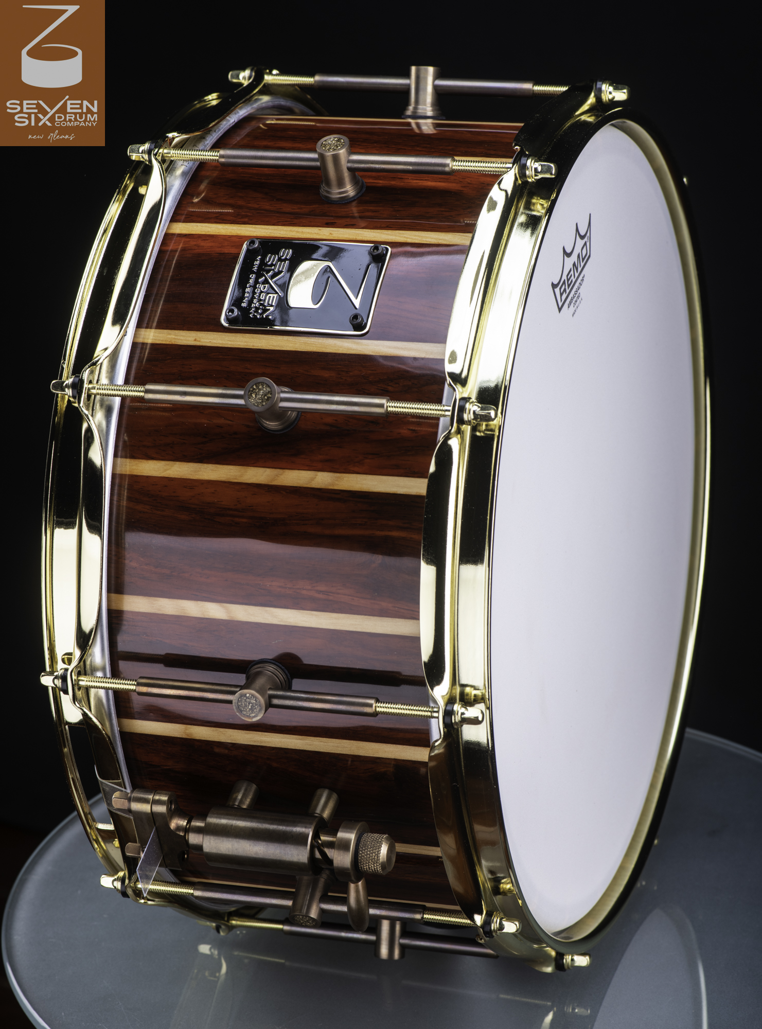 Handmade snare drum featuring a glossy striped wood shell, polished gold hoops, and antique bronze hardware.