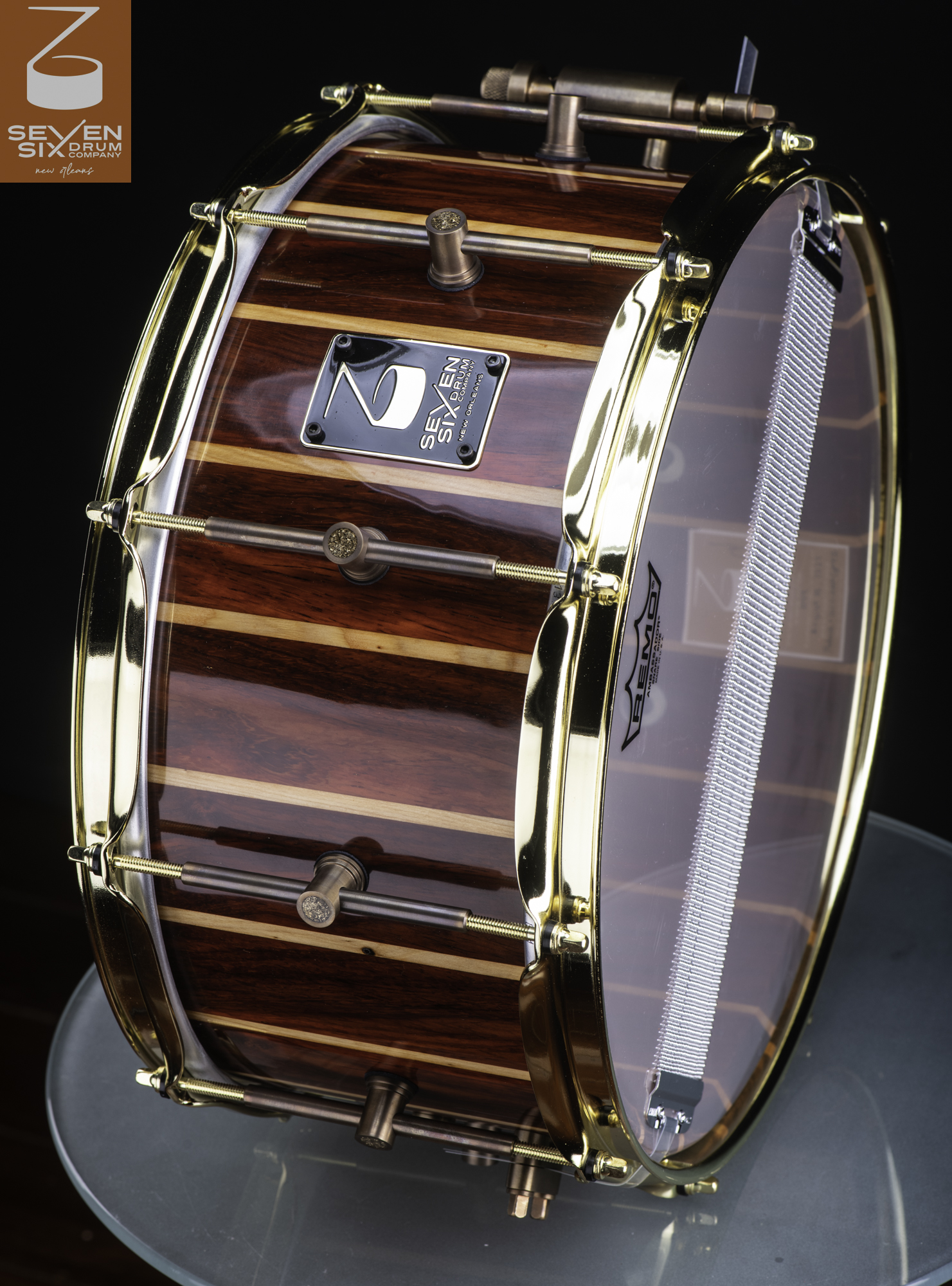 Handmade snare drum with a high-gloss striped wood shell, polished gold hoops, and antique bronze tube lugs.