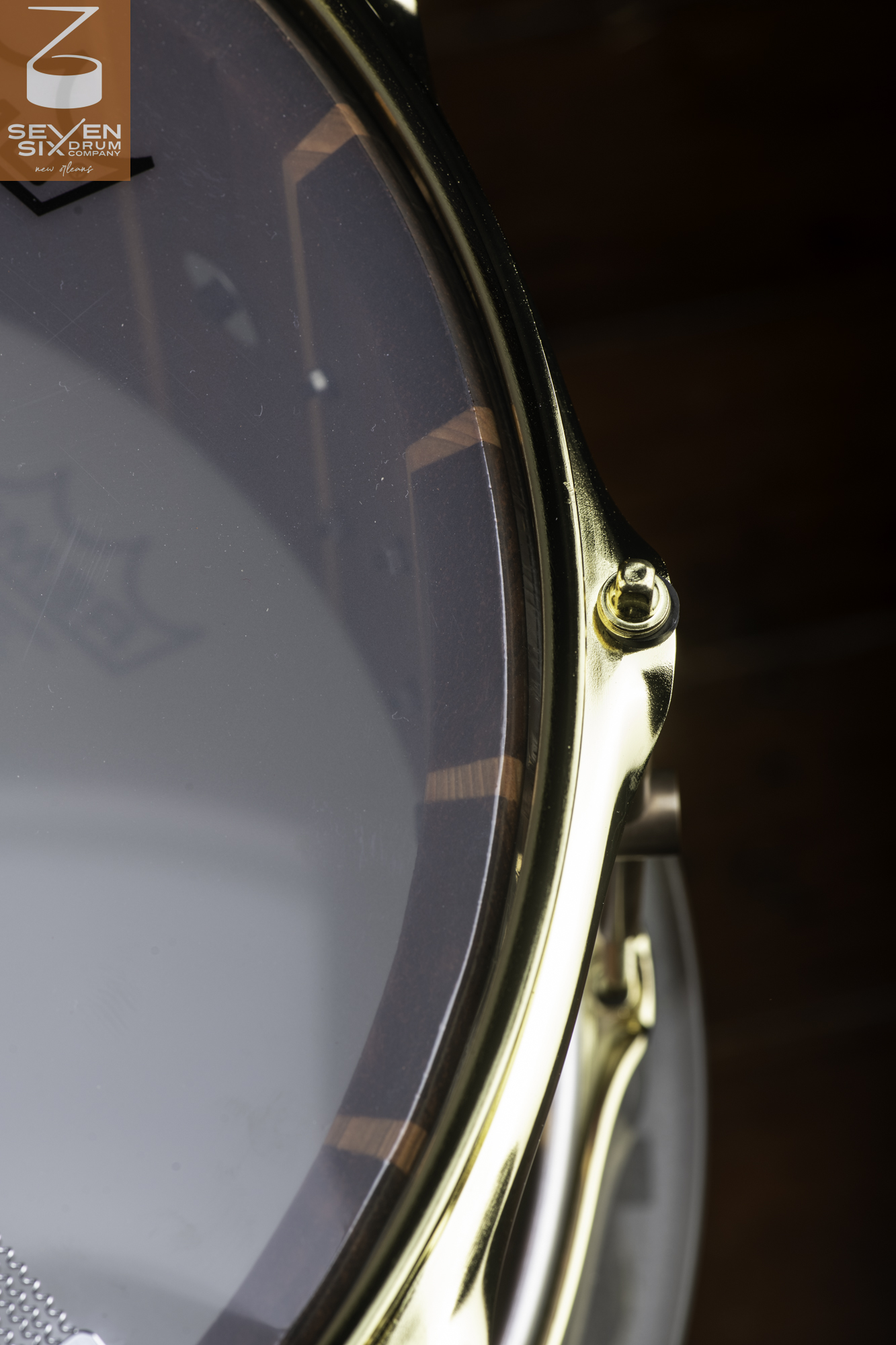 Segmented dark wood snare drum with a gloss finish, polished brass hoop, and gold tension rod hardware.