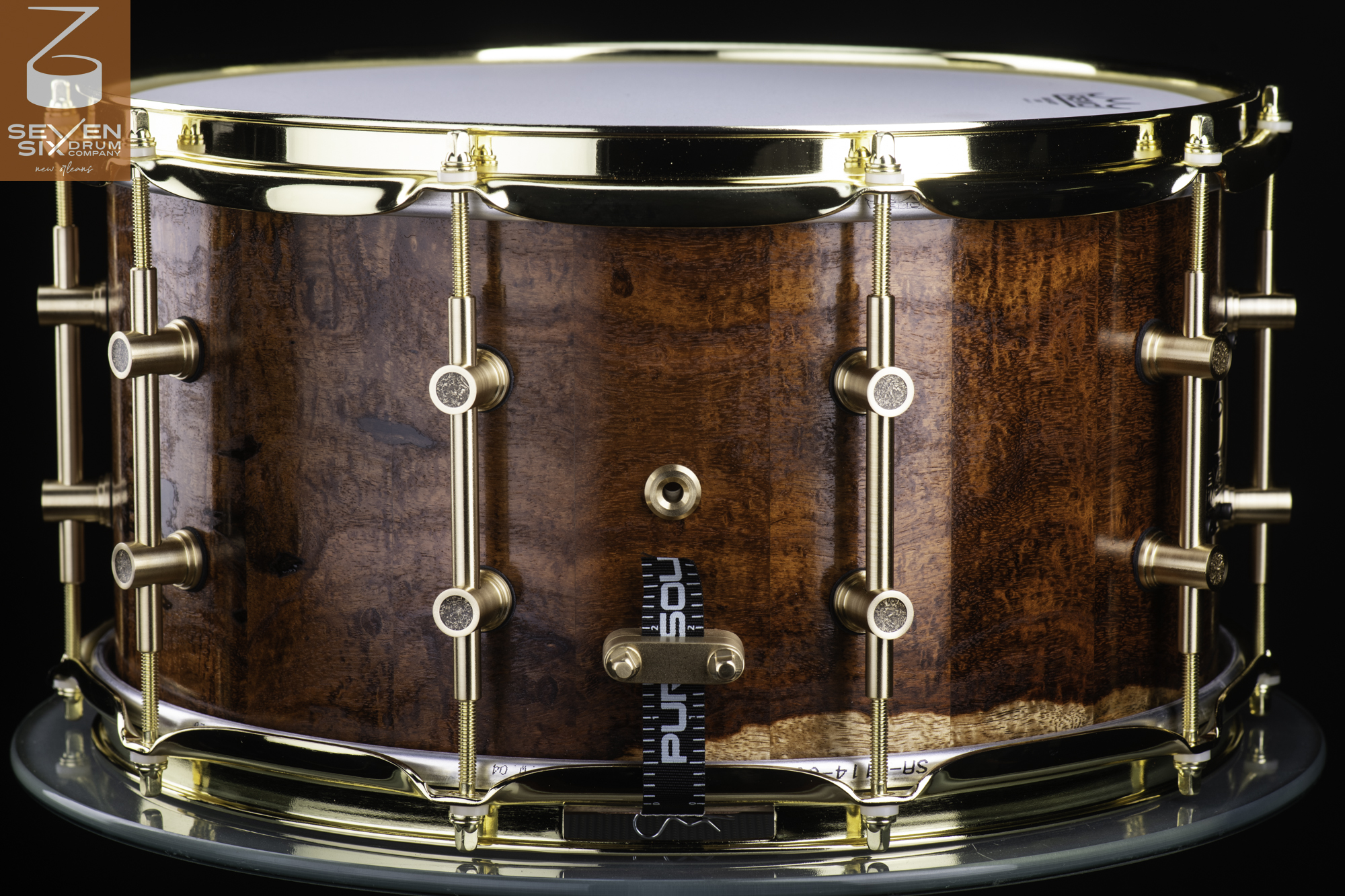 Handmade snare drum with a glossy figured wood shell, polished brass hoops, and brass tube lugs.