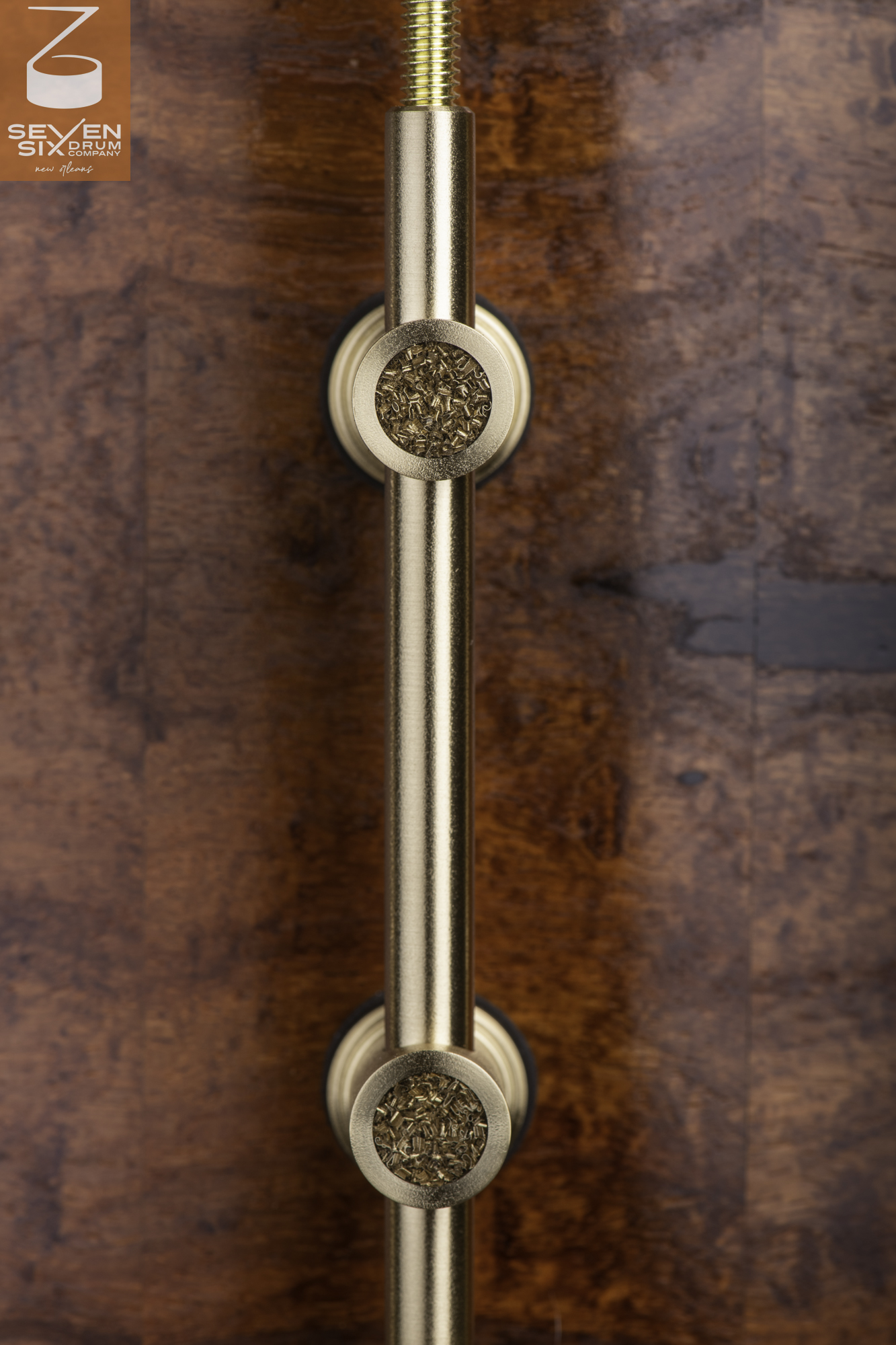Brushed brass tube lug with textured circular inlays mounted on a glossy burl wood snare drum shell.