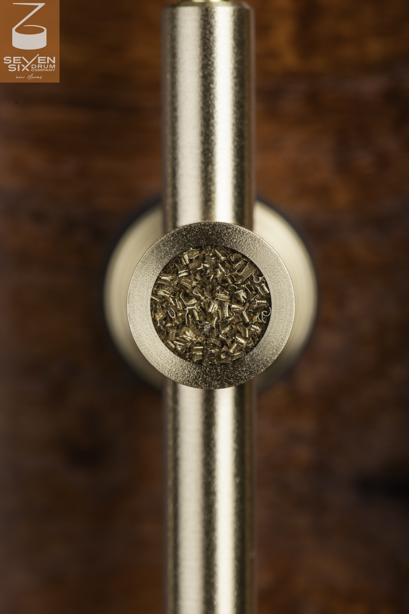 Brushed brass tube lug with a metal shavings inlay mounted on a reddish-brown wood snare drum shell.