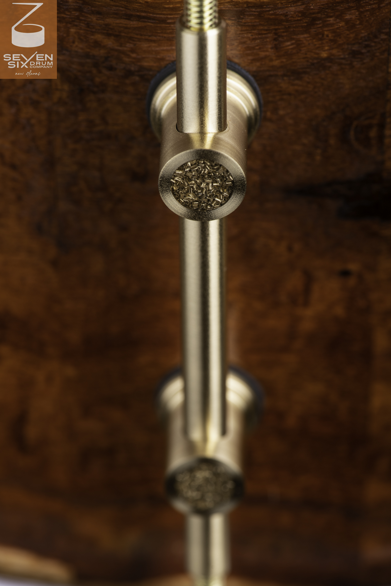 A brushed brass tube lug with textured inlay mounted to a polished dark wood snare drum shell.