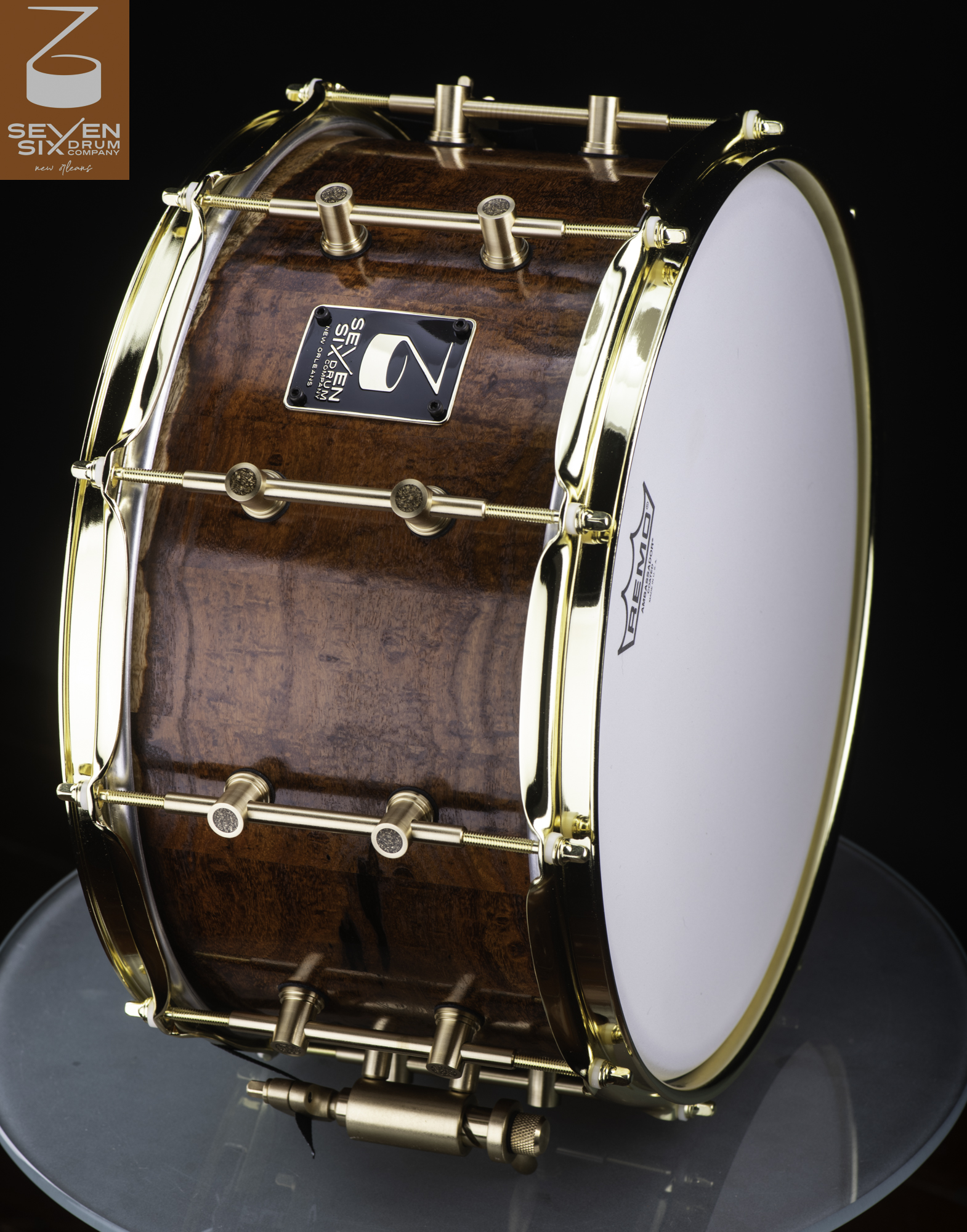 Handmade snare drum with a glossy figured wood shell, polished gold hoops, and brass tube lugs.