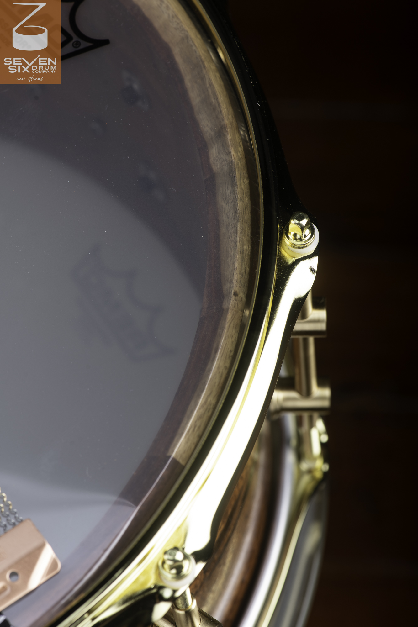 Handmade dark wood snare drum featuring a polished brass hoop, brass tube lugs, and a clear bottom head.